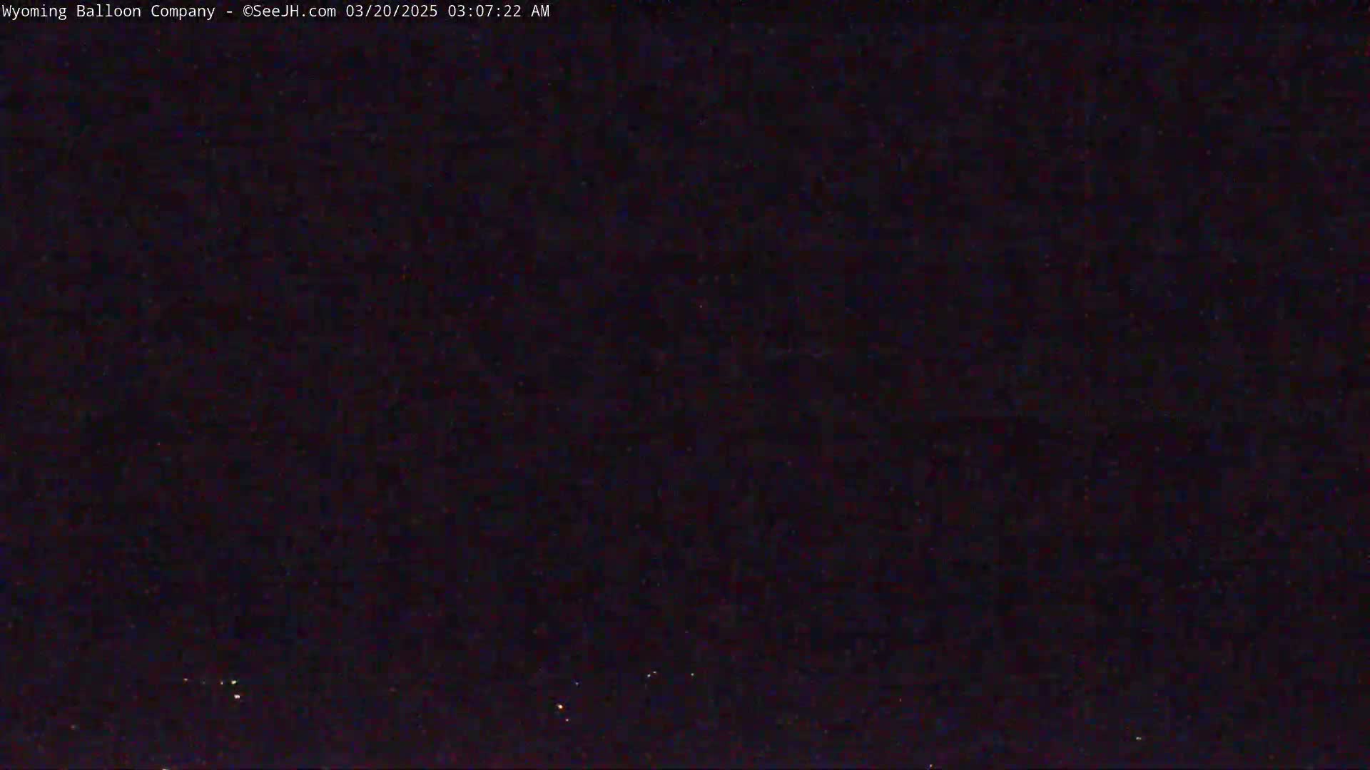 A dark, nighttime image shows a mostly clear sky with a few faint lights visible.