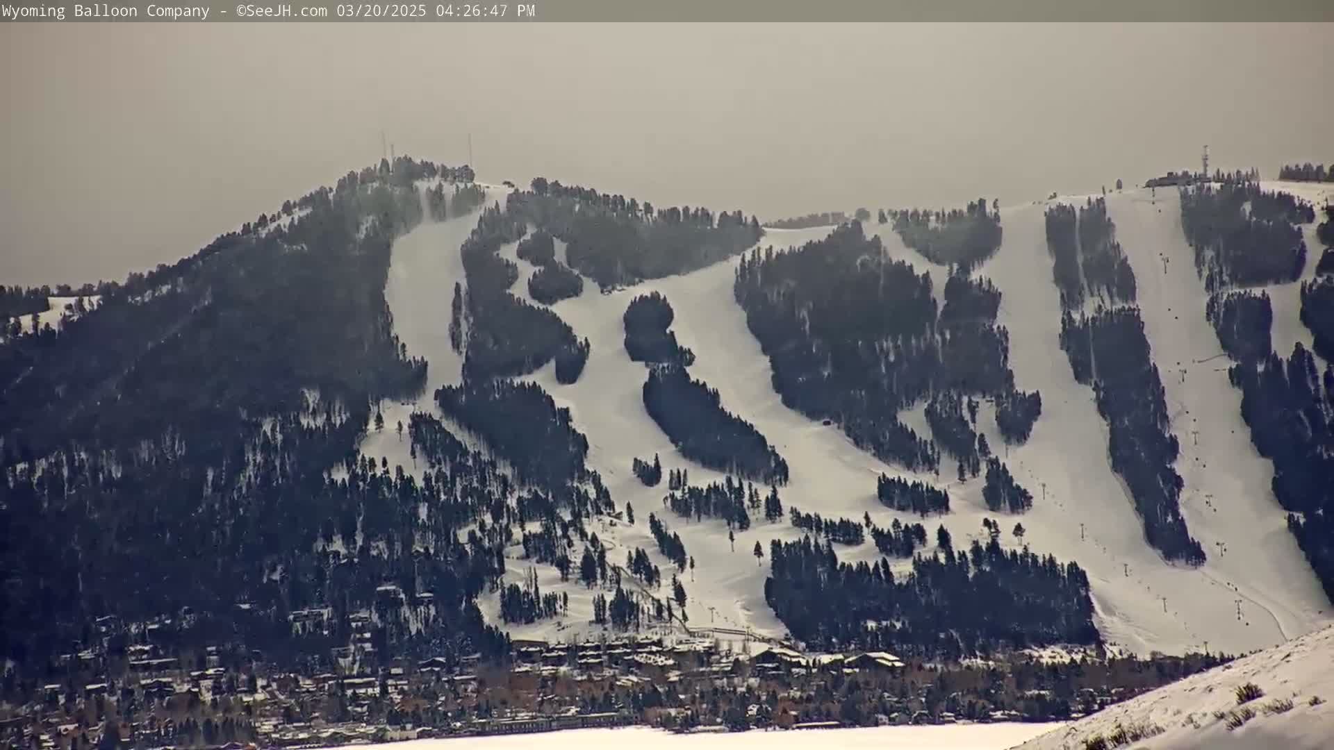 A snow-covered ski resort with numerous ski runs is visible under a hazy sky.