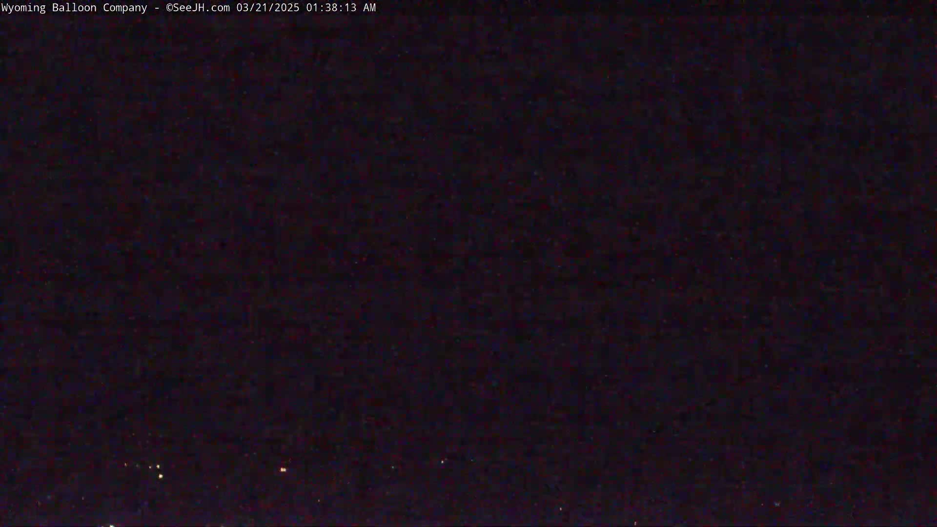A dark, nighttime scene shows a mostly clear sky with a few faint lights visible on the horizon.