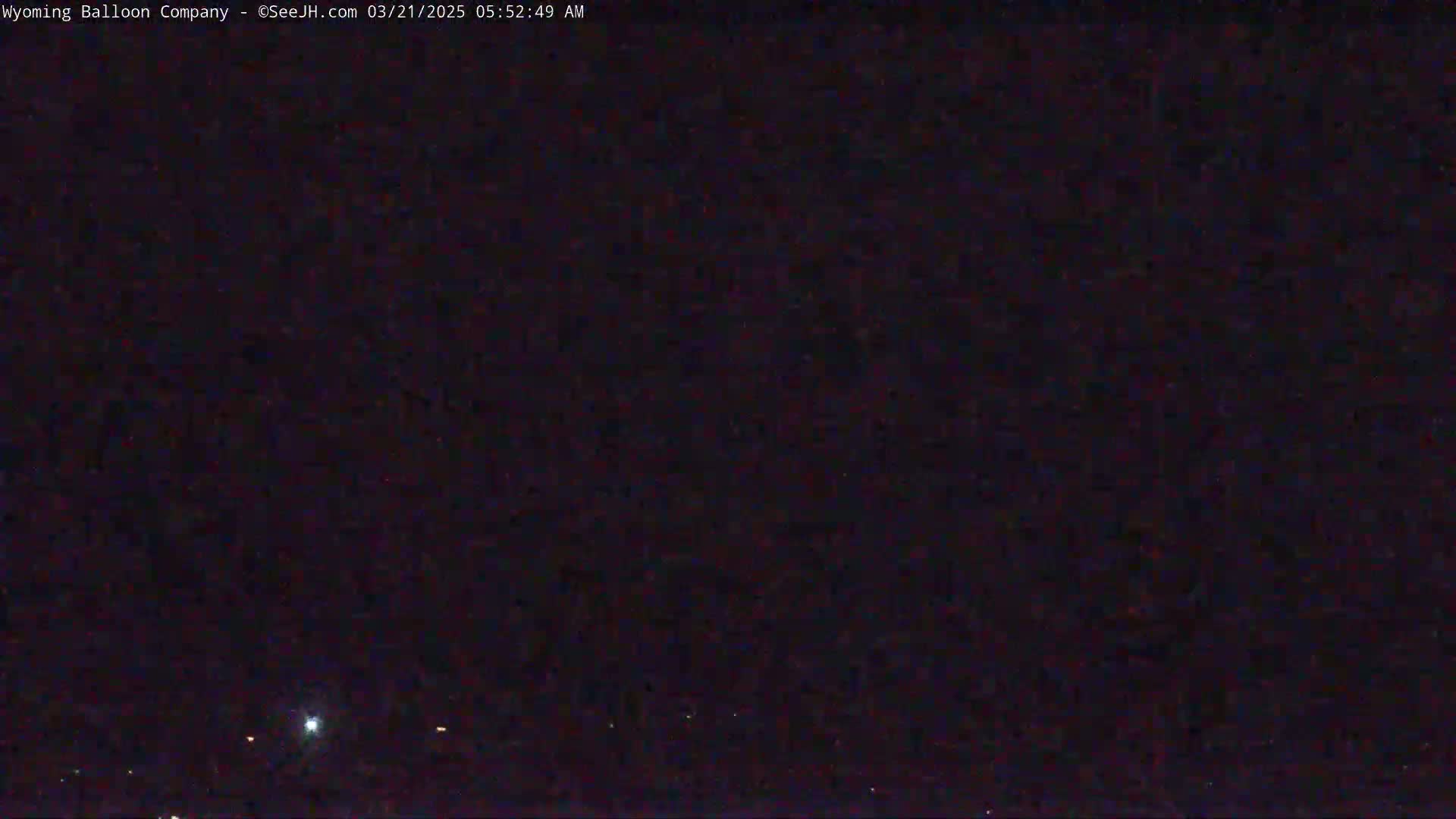 A dark nighttime scene shows a few faint lights on the horizon under a mostly clear, dark sky.