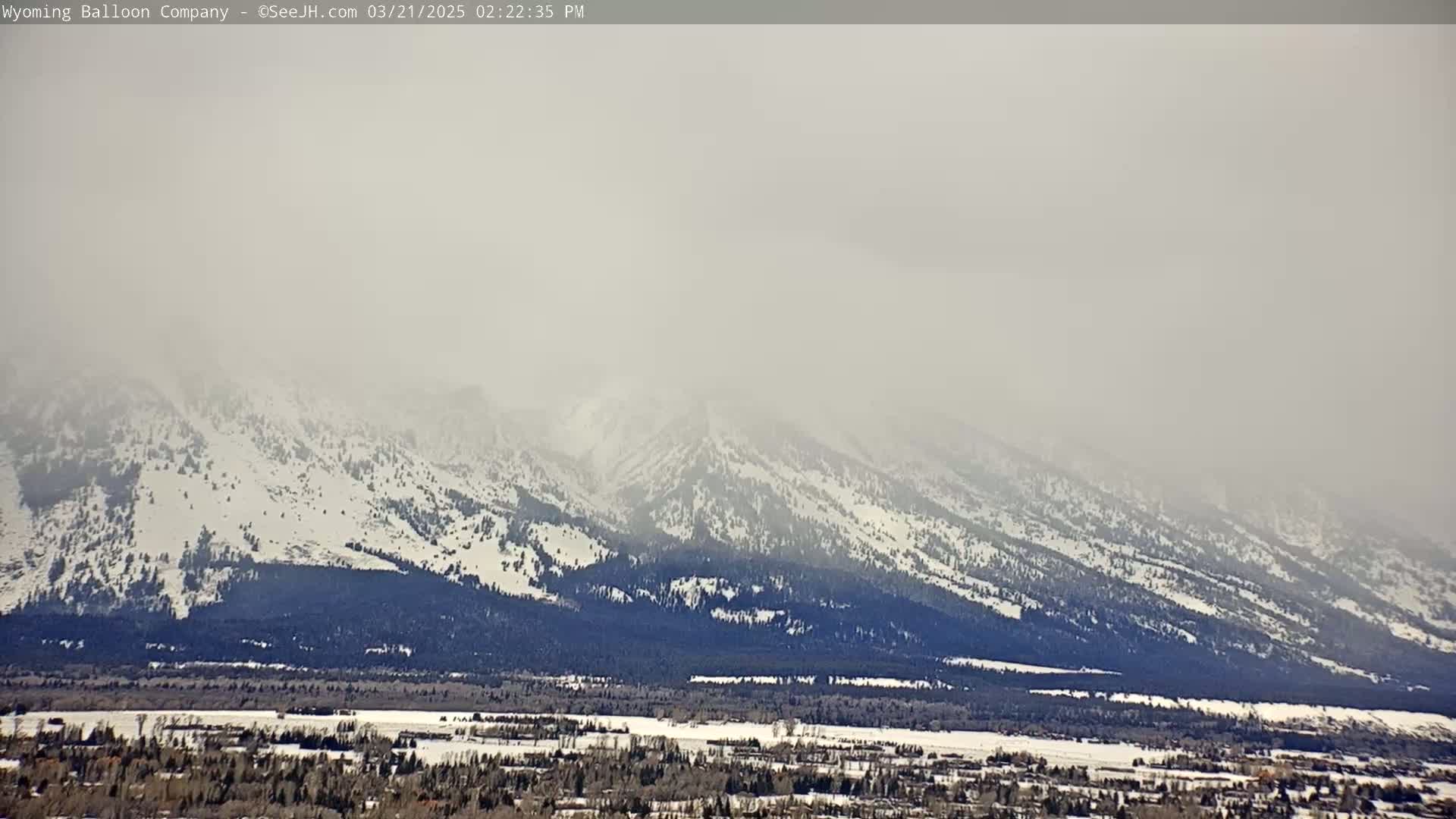 Snow-covered mountains are visible through a hazy atmosphere over a snow-dusted valley.