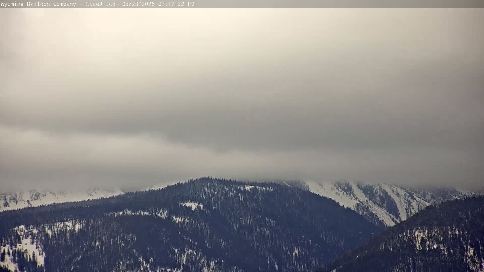 A snow-covered mountain range is partially obscured by a thick layer of fog or low clouds.