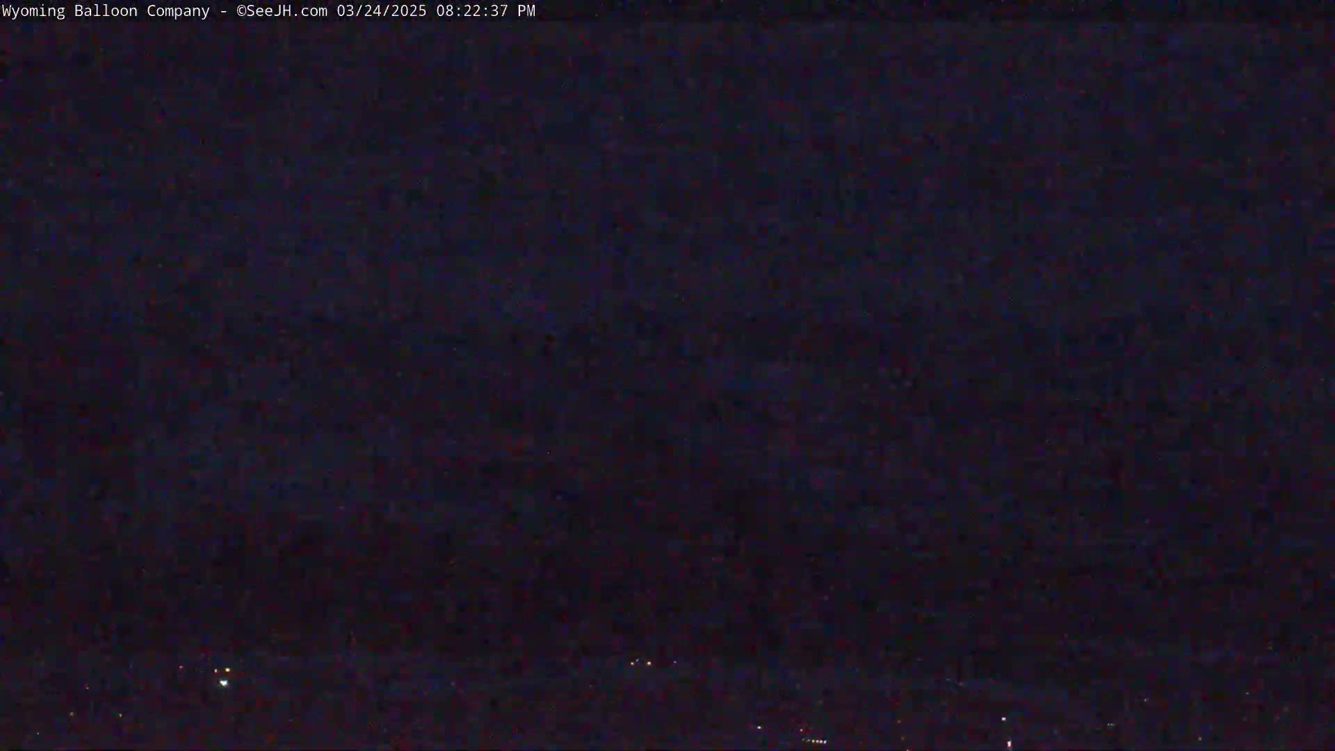 A dark, nighttime scene shows a mostly clear sky with a few faint lights visible on the horizon.