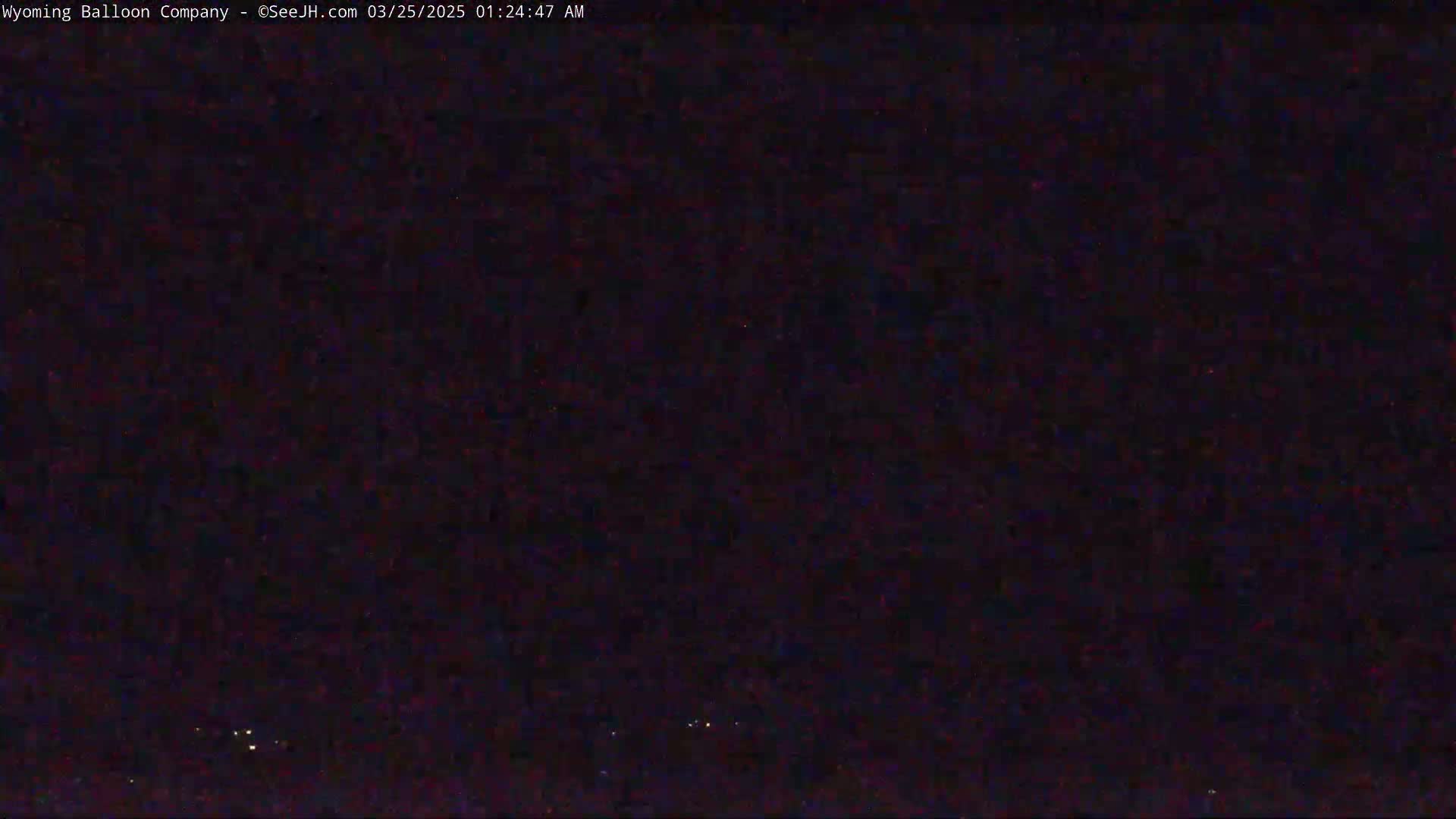 A dark, nighttime image shows a few faint lights in the distance under a clear, dark sky.