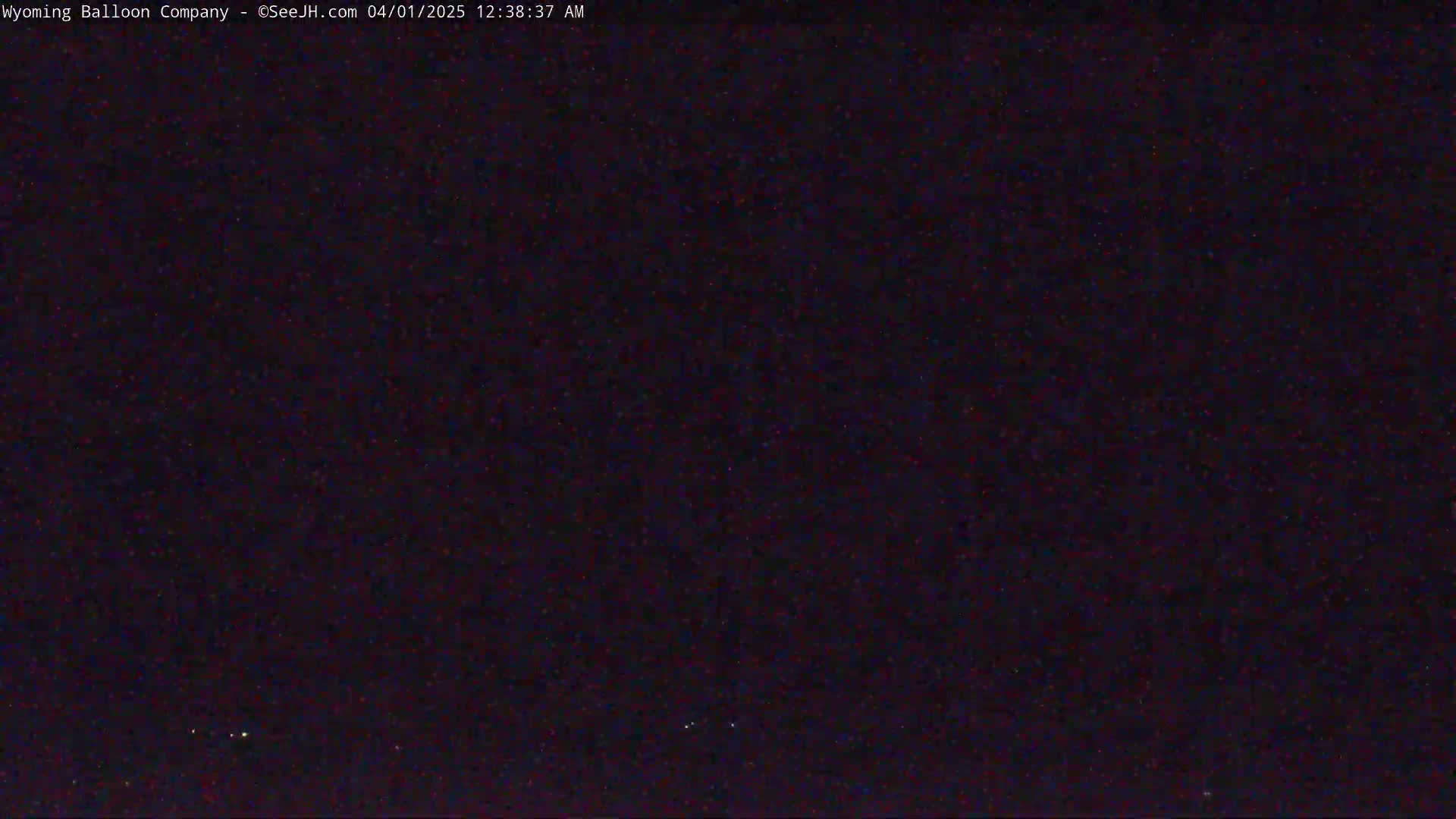 A dark, nighttime image shows a mostly clear sky with a few faint lights visible in the distance.