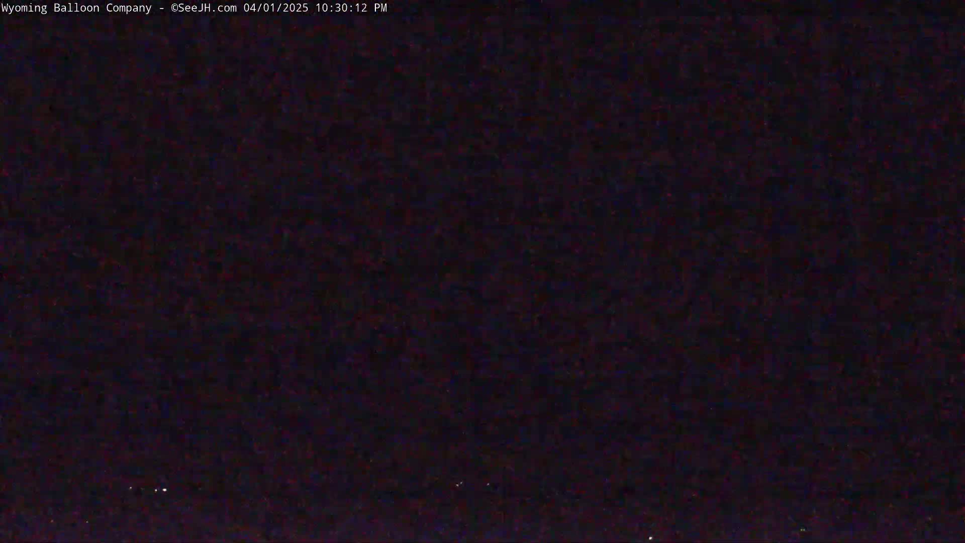 A dark, nighttime scene shows a few faint lights in the distance under a clear sky.