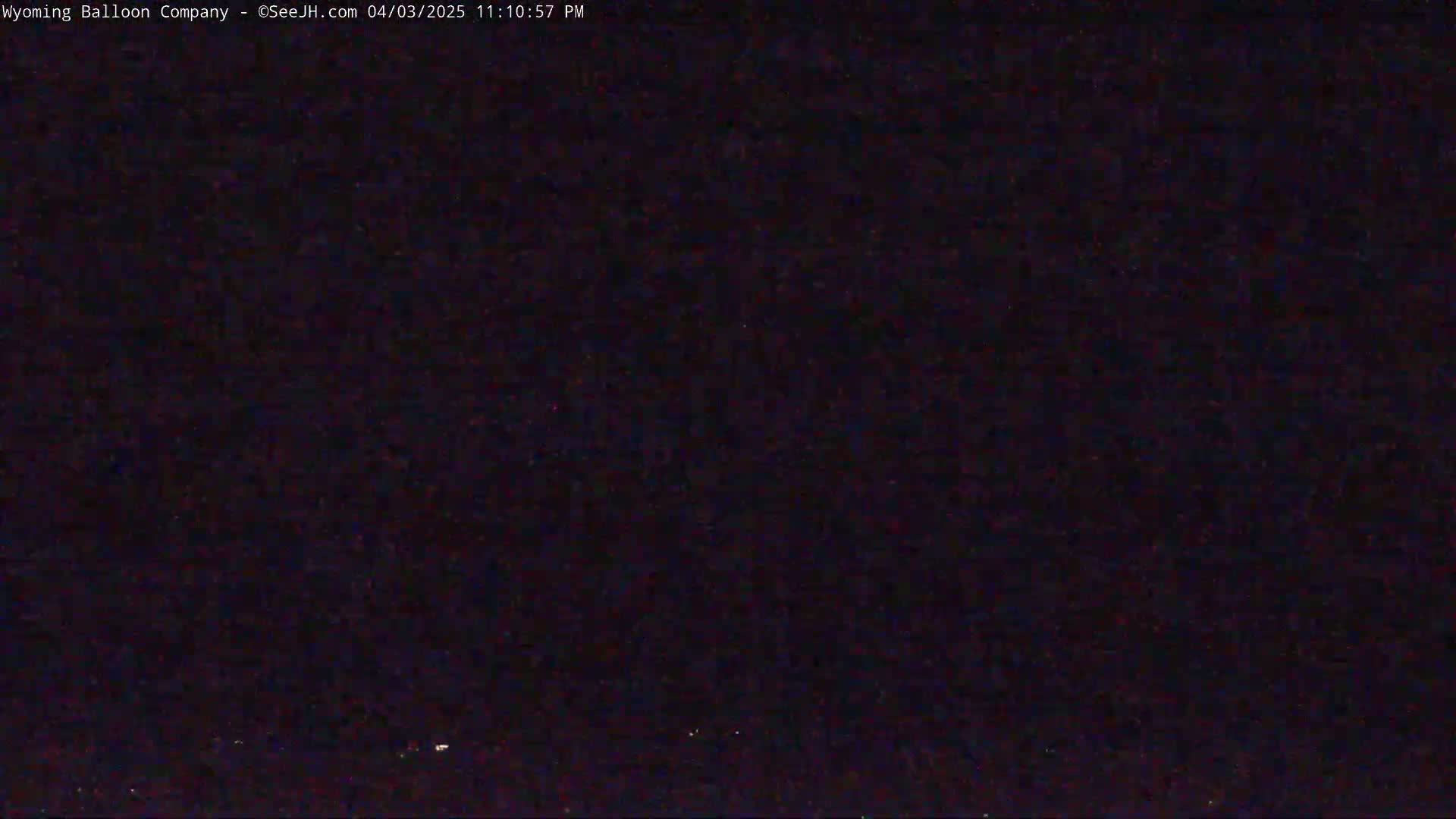 A nighttime, dark image shows a few faint lights on the horizon under a clear, dark sky.