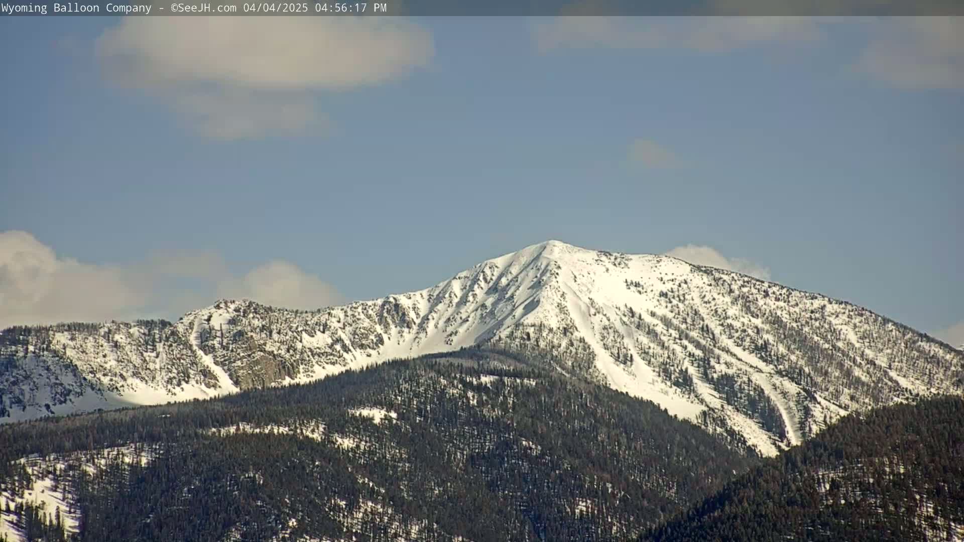 A snow-capped mountain range is visible under a mostly clear, light blue sky with a few scattered clouds.