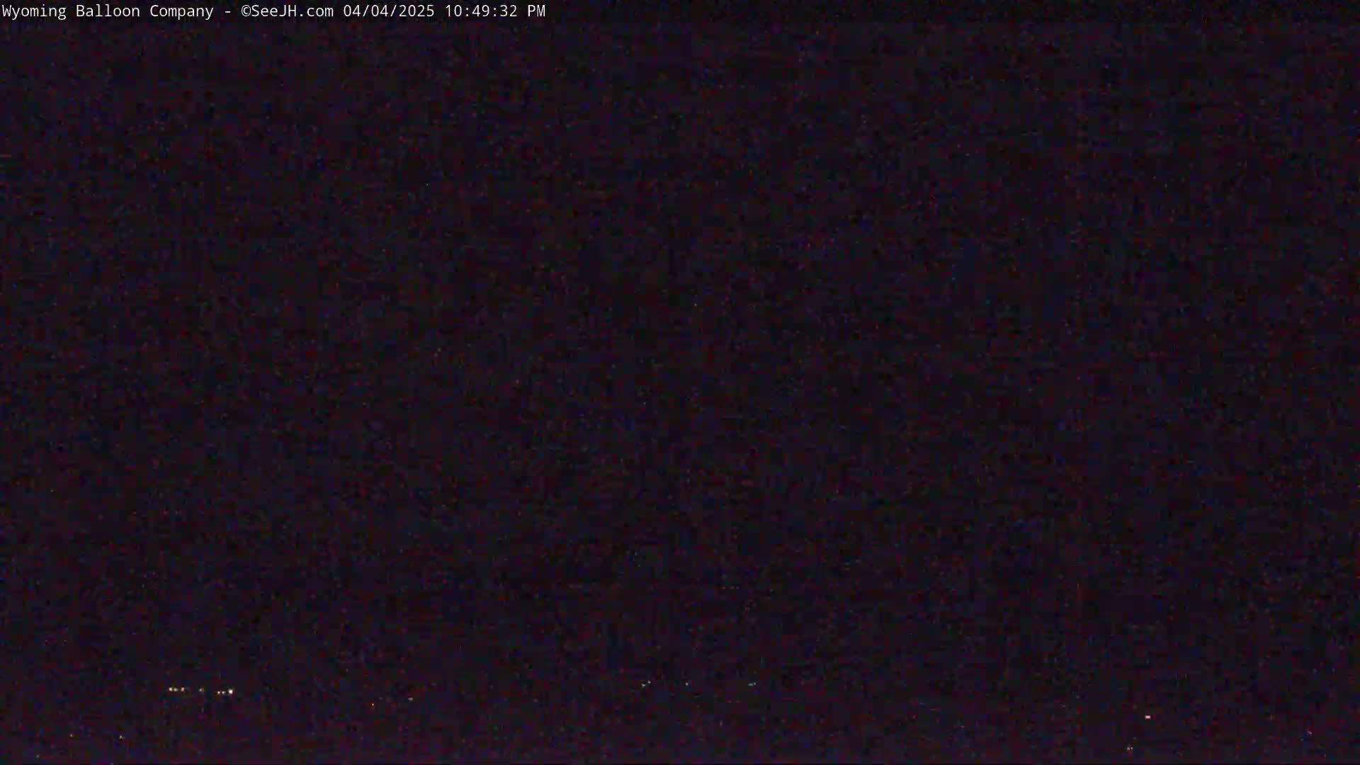 A nighttime, dark image shows a few faint lights on the horizon under a clear, dark sky.