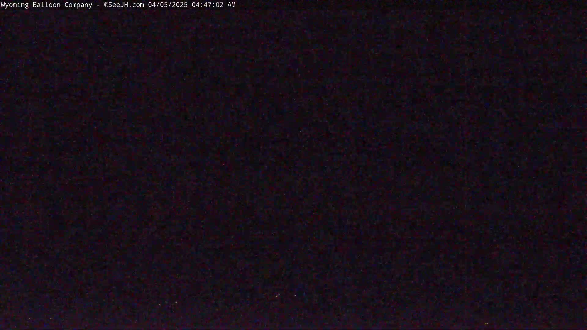 A dark, nighttime scene shows a mostly clear sky with a few faint lights visible on the horizon.