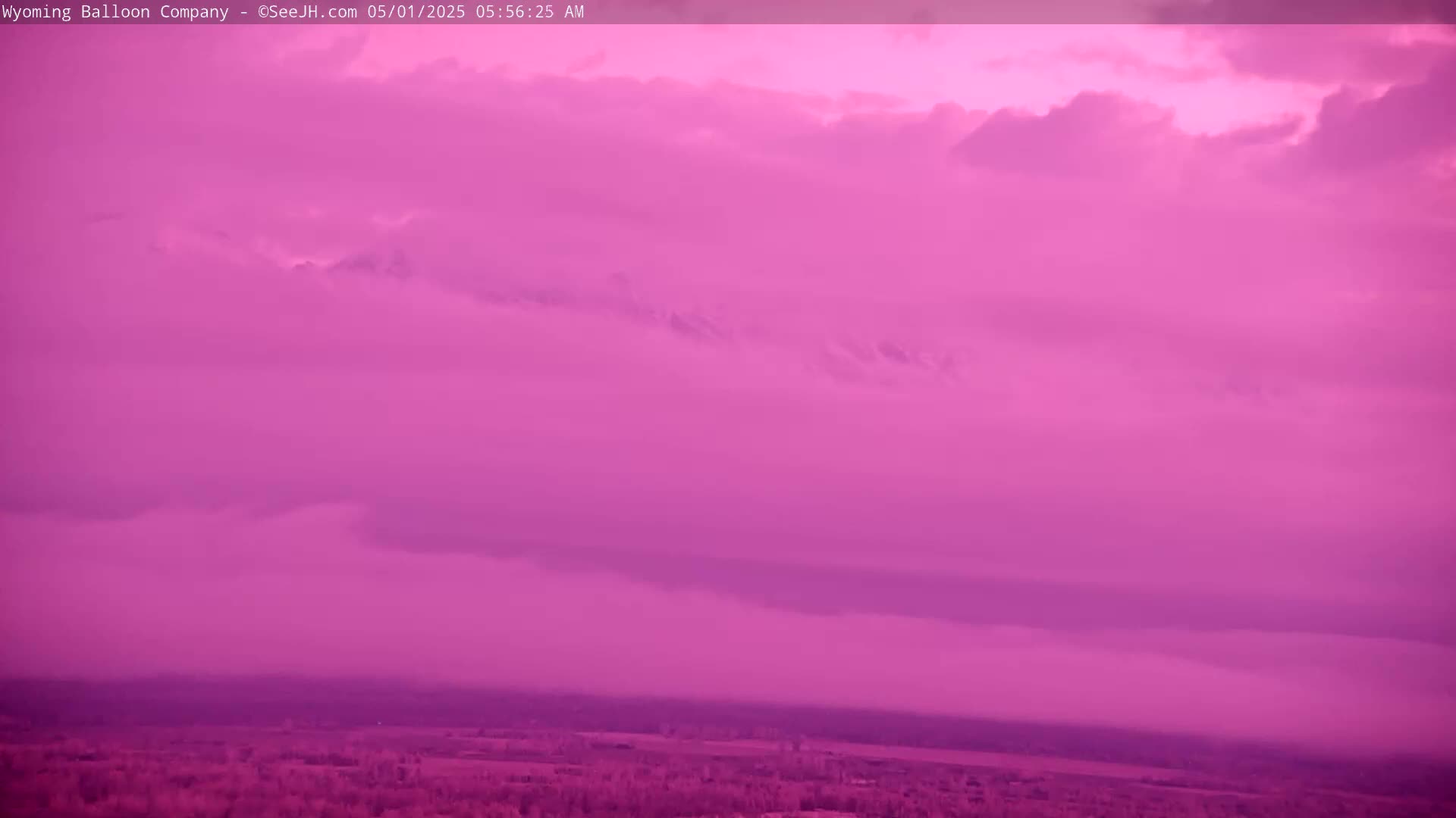 A pink-hued sky filled with clouds sits above a flat expanse of land.