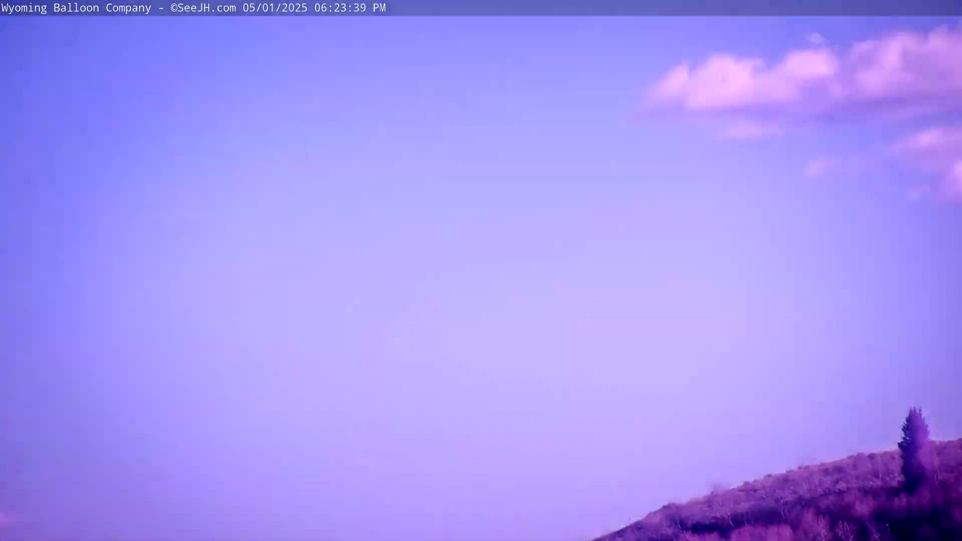 A partly cloudy, lavender-hued sky is visible above a gently sloping, dark-purple hillside with sparse vegetation.