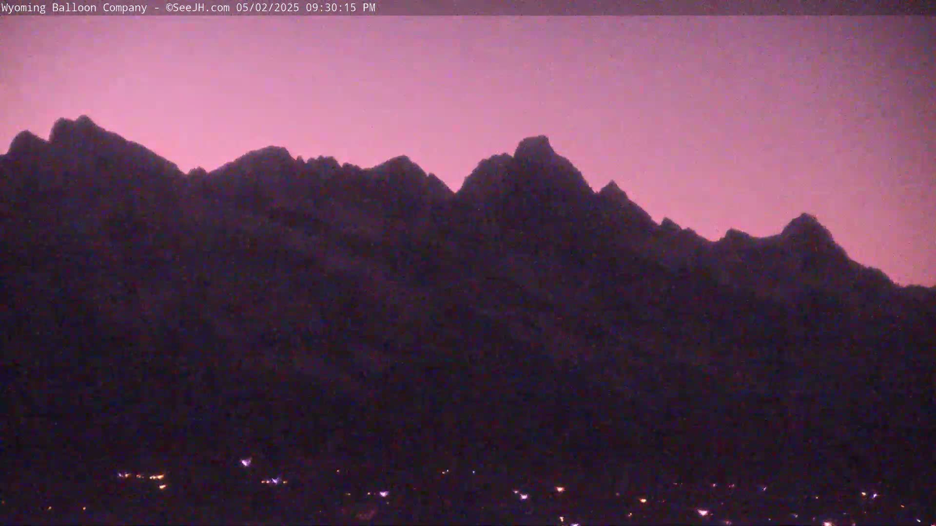 Silhouetted mountains are visible against a dusky pink sky at twilight, with a few small lights scattered at the base.