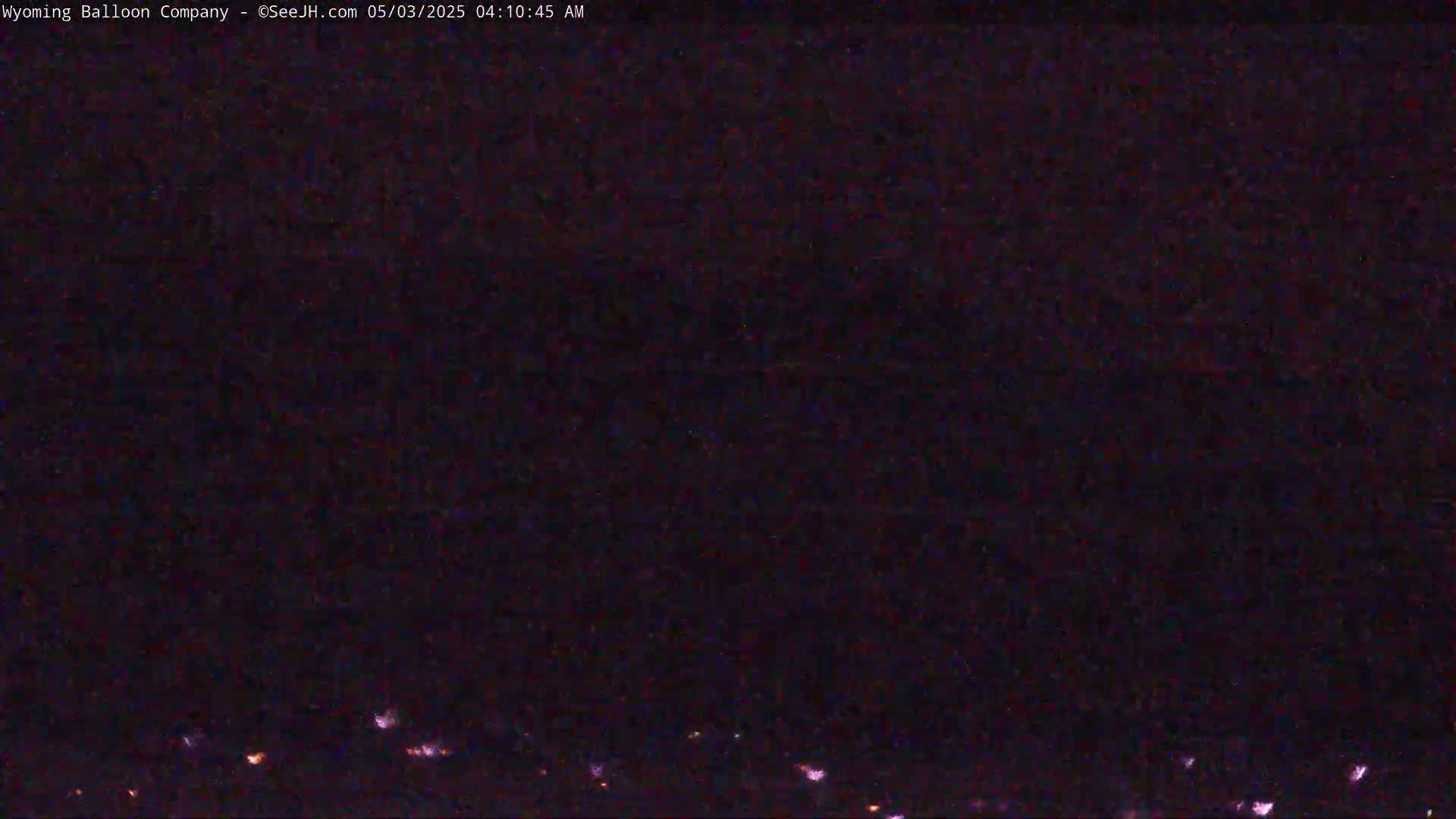 A dark, nighttime scene shows a distant line of faint, orange lights on the horizon under a mostly clear, dark sky.