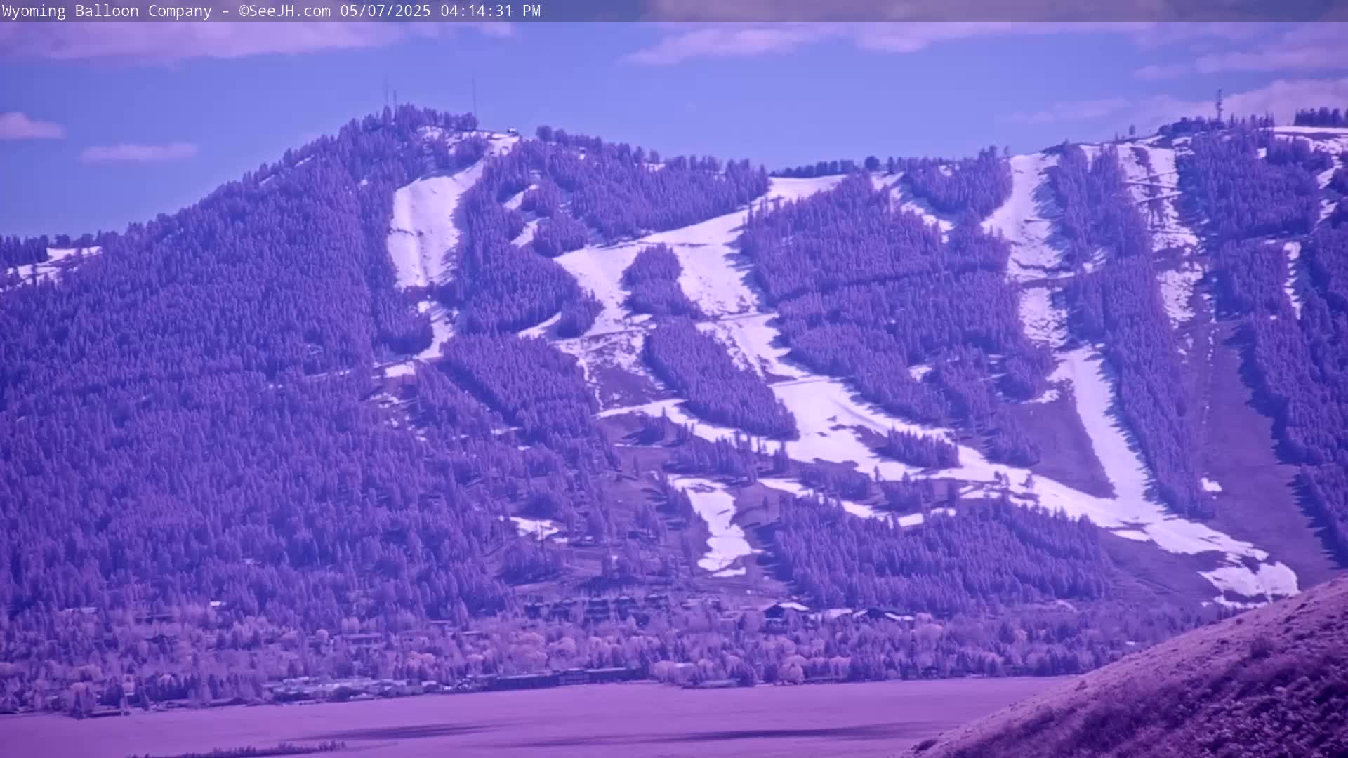 A snow-dusted mountainside, covered in evergreen trees and ski runs, is visible under a clear blue sky.
