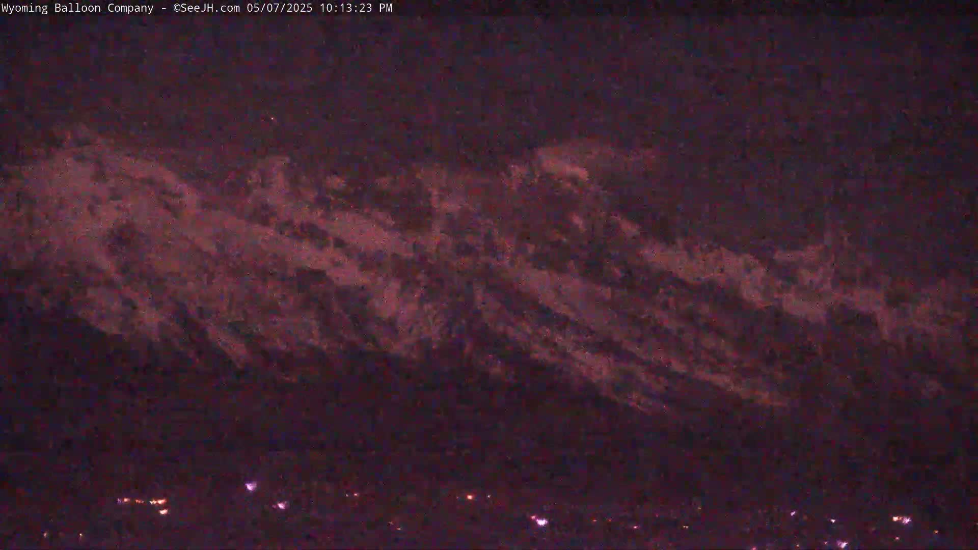 A nighttime view shows a dark mountain range silhouetted against a purplish-pink sky.