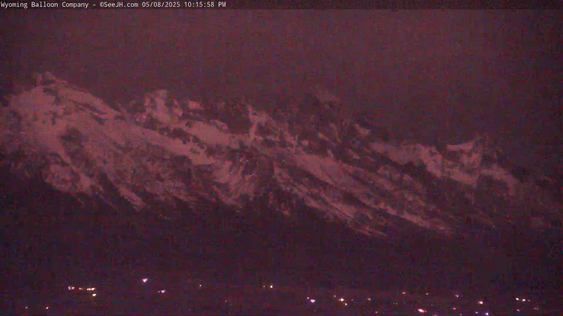 A snow-capped mountain range is visible at twilight, with a few small lights illuminating the bottom of the frame.
