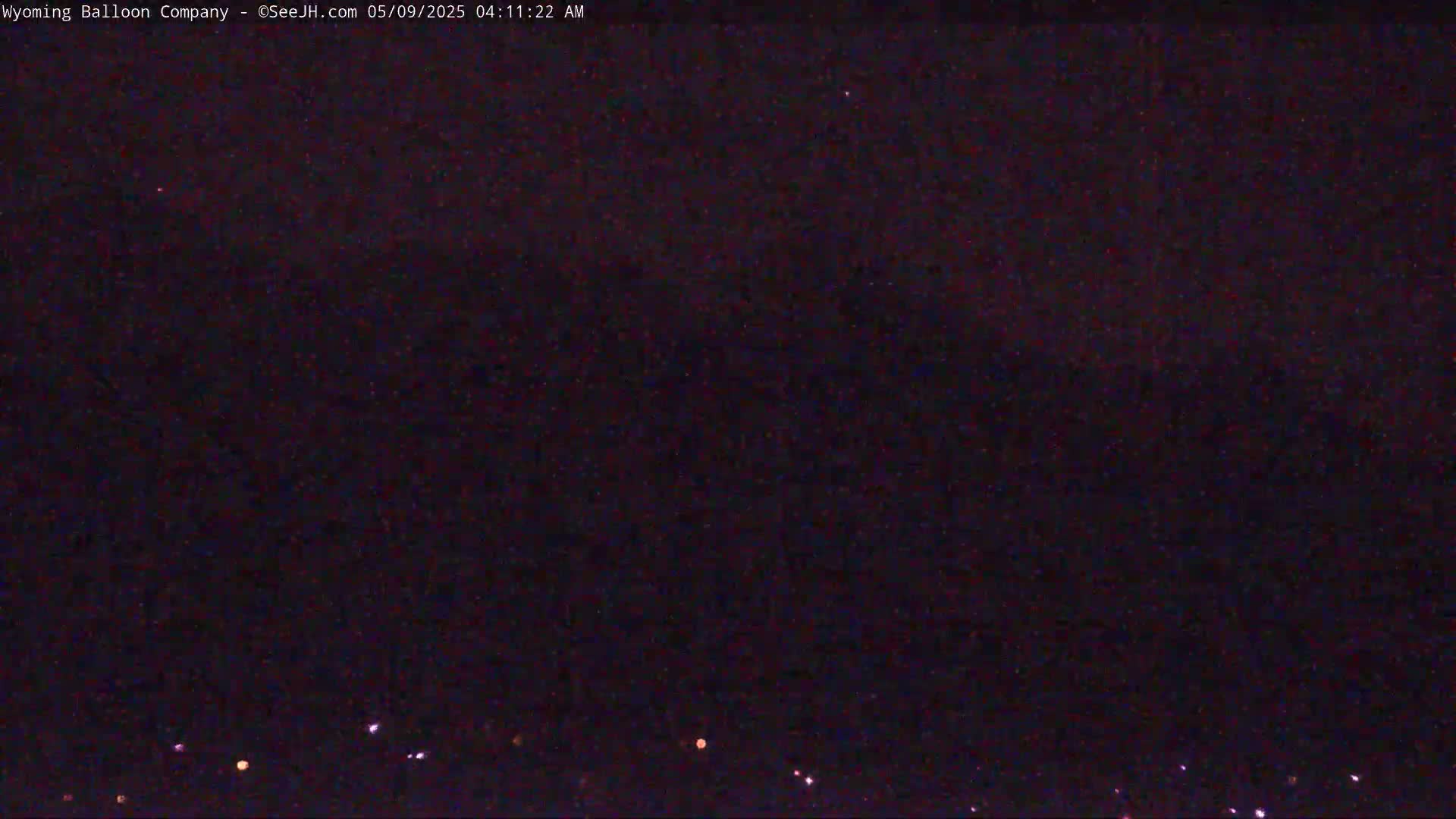 A nighttime, dark image shows a few distant lights on the horizon under a mostly clear sky.