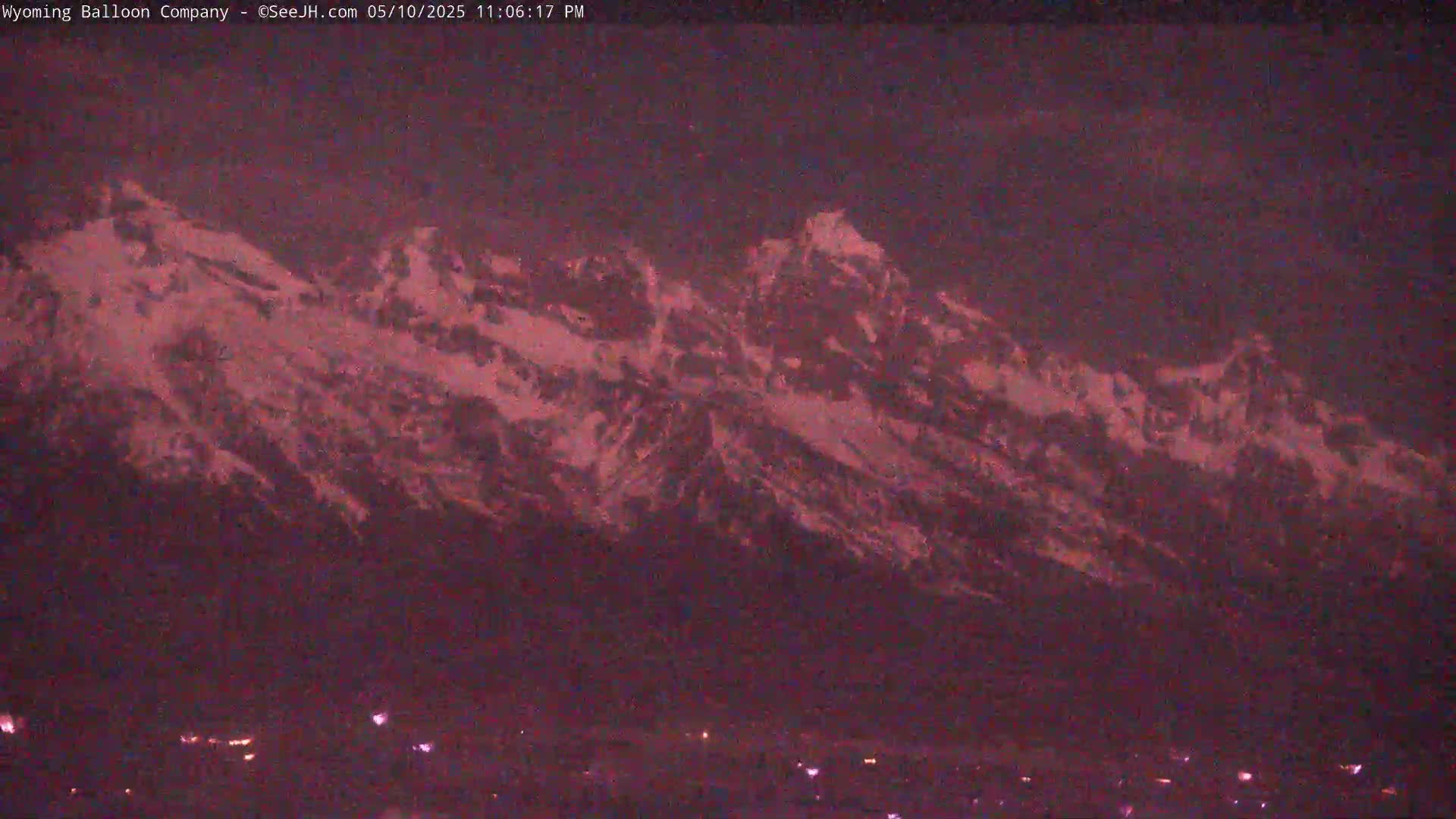 A snow-capped mountain range is visible at night under a dark, reddish-purple sky, with a few small lights illuminating the base.