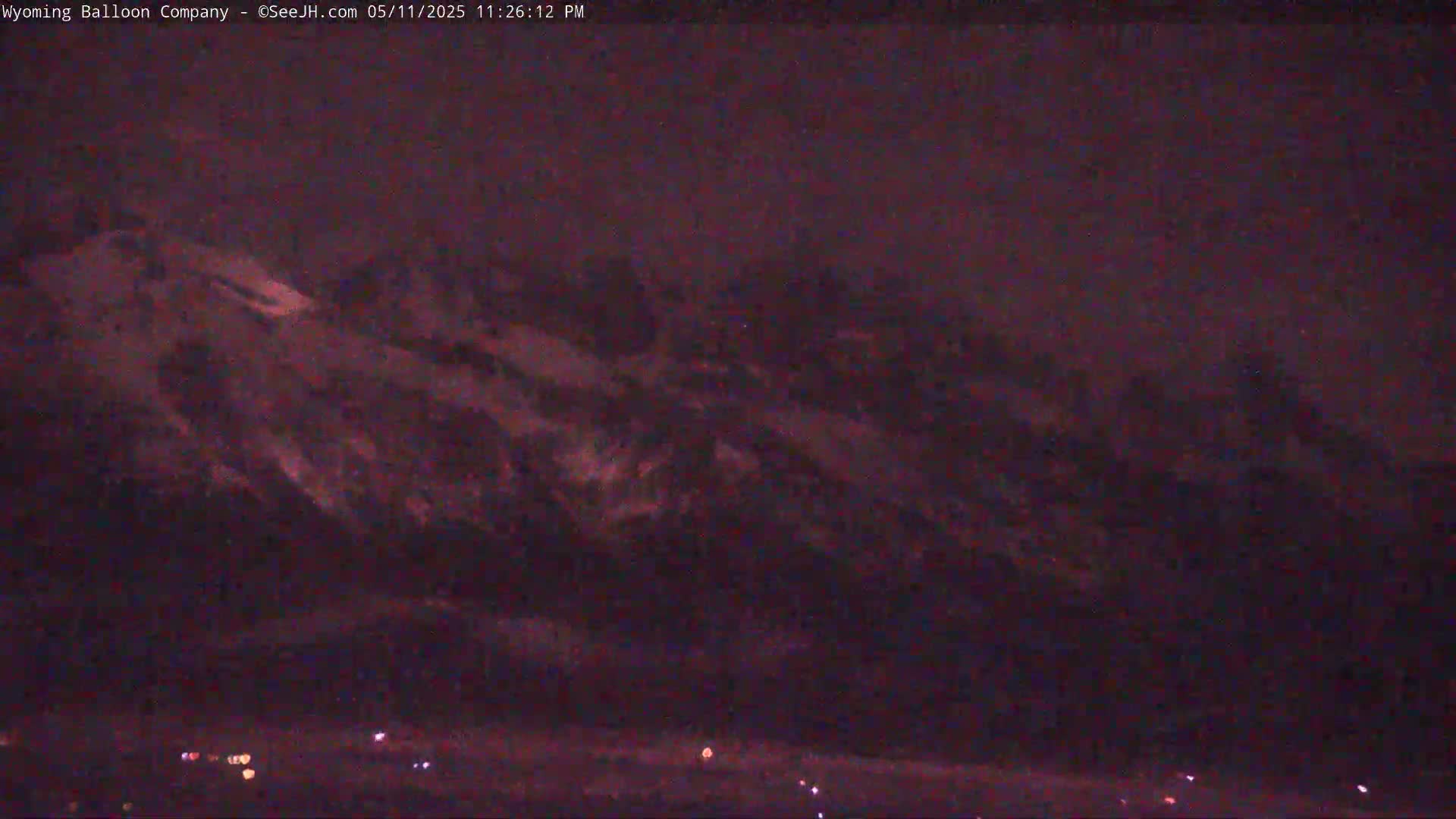 A dark, nighttime view shows a snow-covered mountain range under a clouded sky.