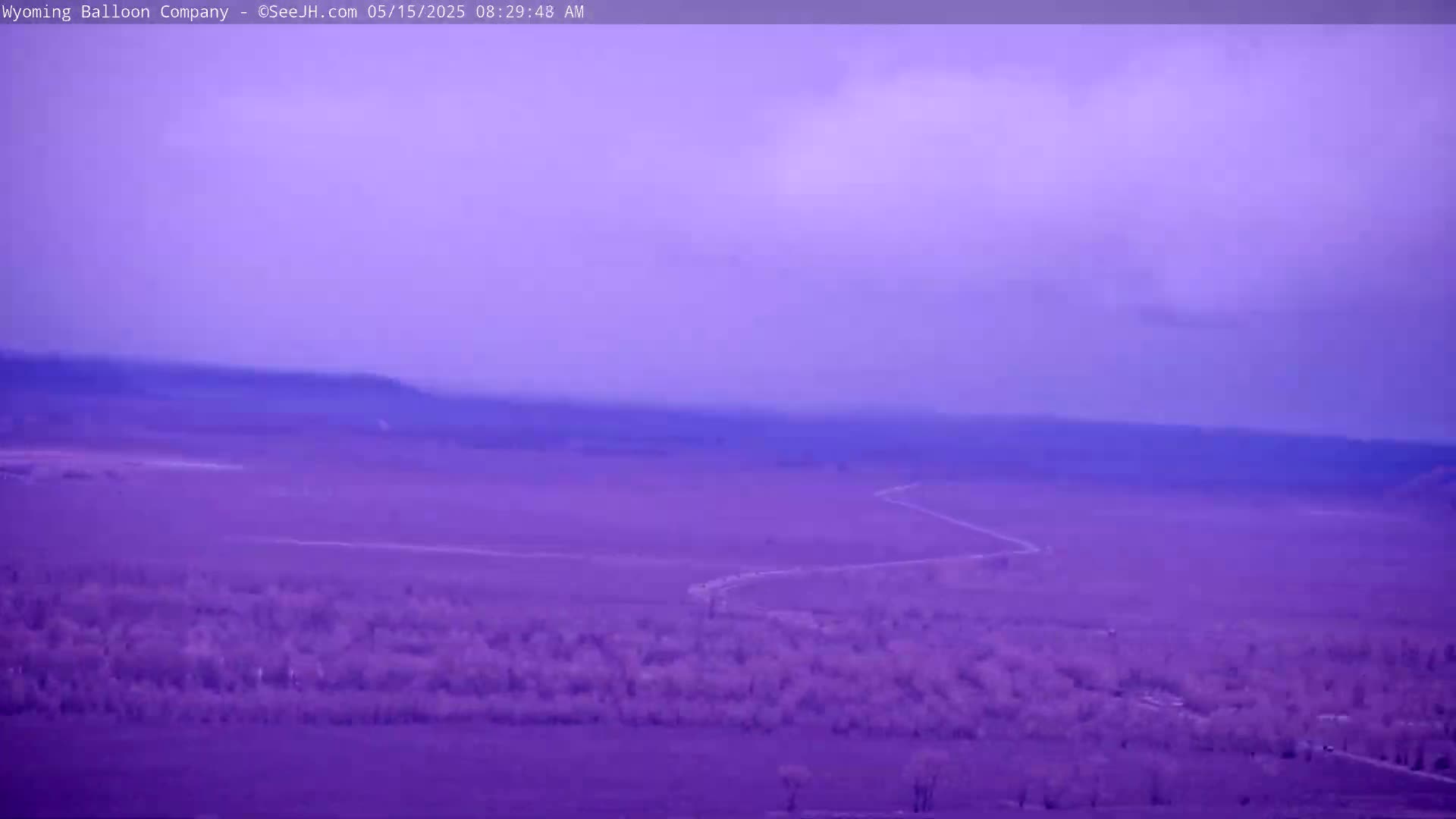 A winding road cuts through a flat, purple-hued landscape under an overcast sky.