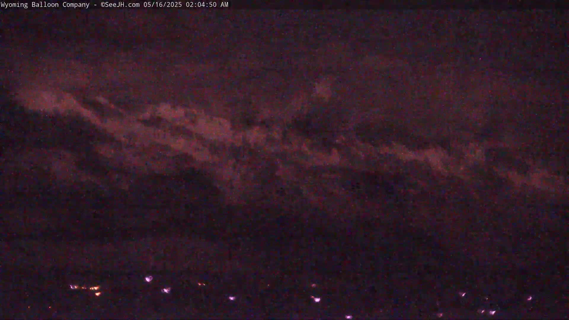 A dark, nighttime sky shows streaks of purplish-pink clouds above a faint line of distant lights.