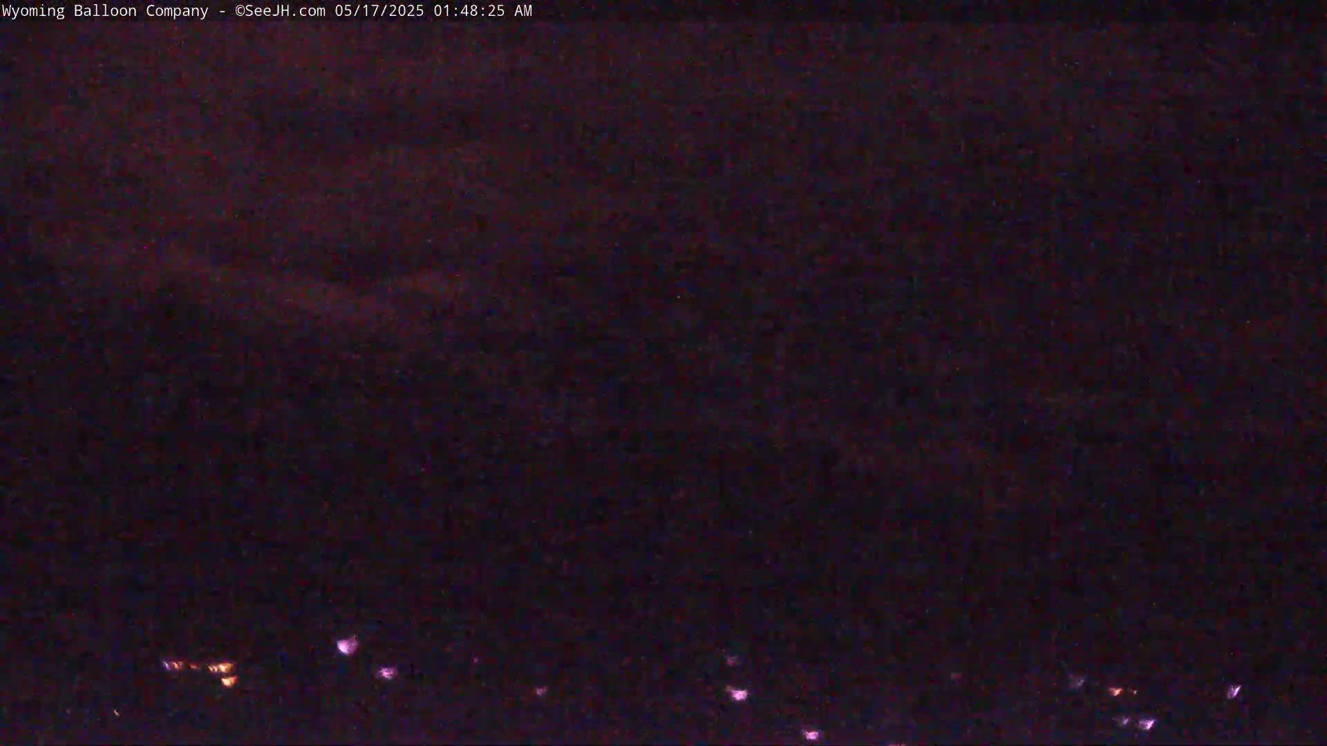 A dark, nighttime scene shows a few distant lights on the horizon under a mostly cloudy sky.