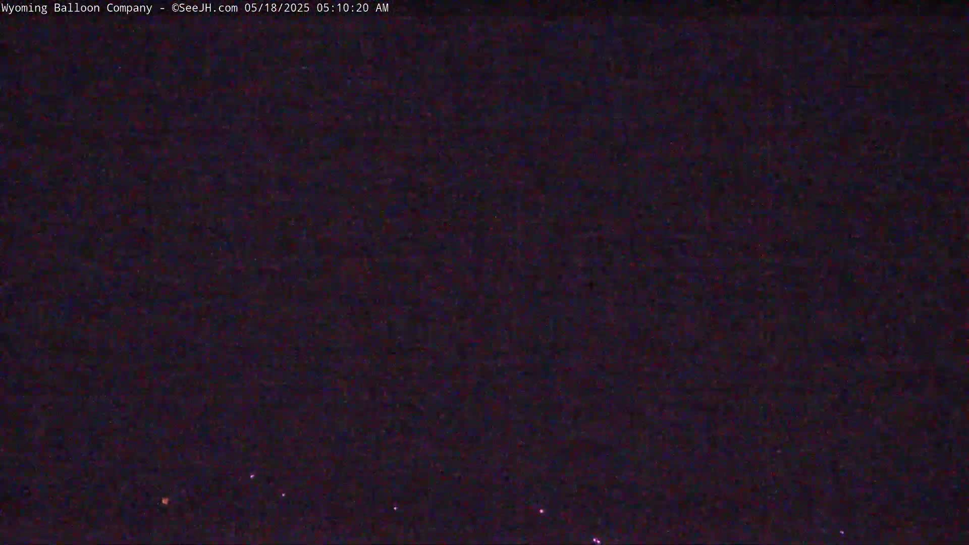 A dark, nighttime scene shows a few small, faint lights in the distance under a clear, dark sky.