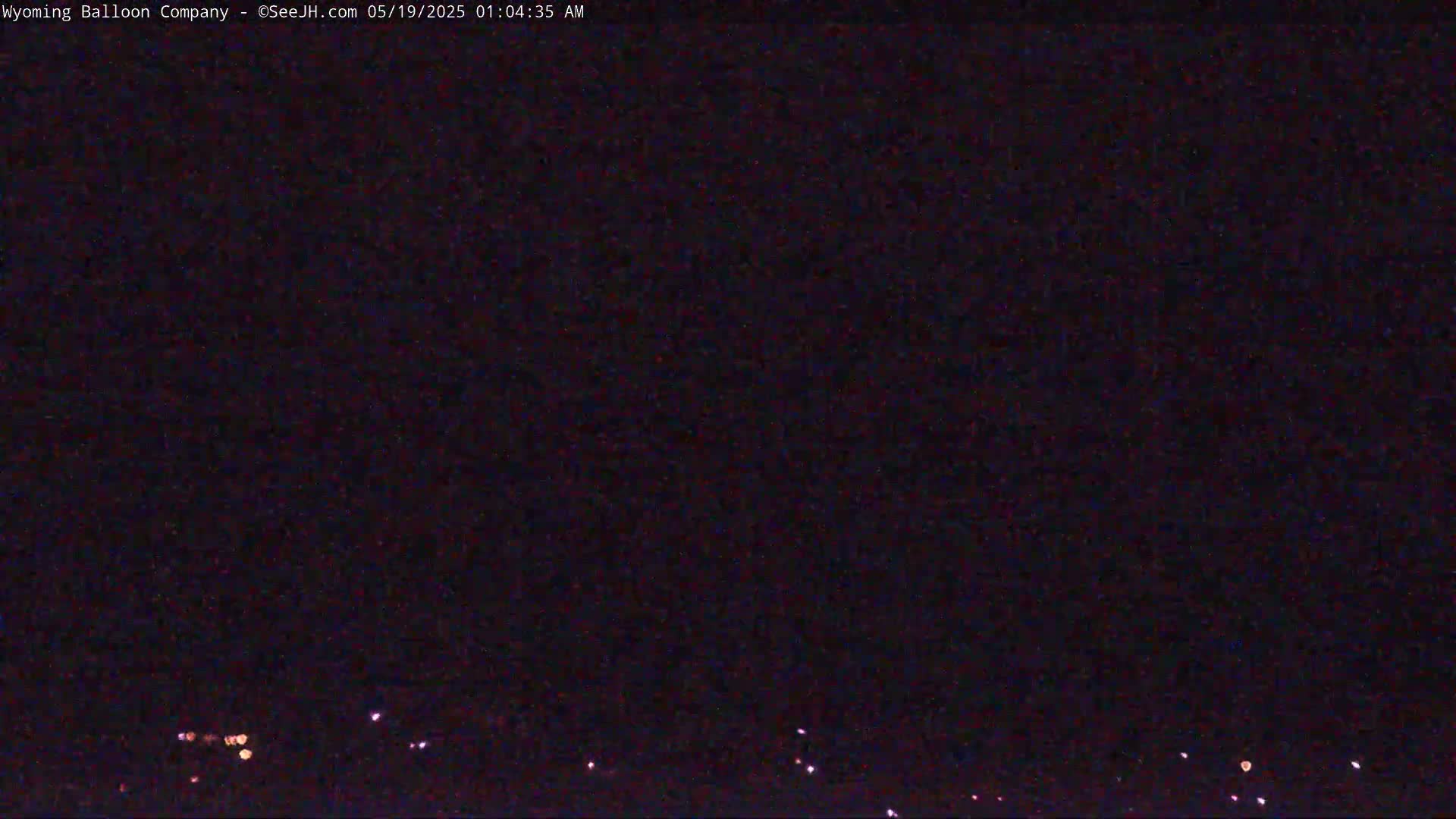A nighttime, dark image shows a few small, faint lights on the horizon.