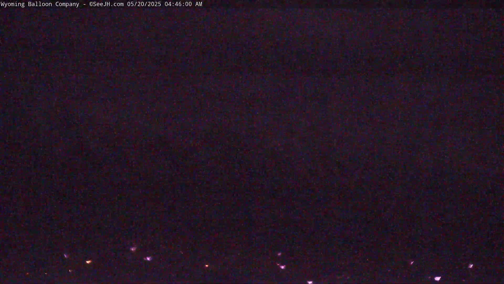 A dark, nighttime scene shows a few faint lights on the horizon under a mostly clear, dark sky.