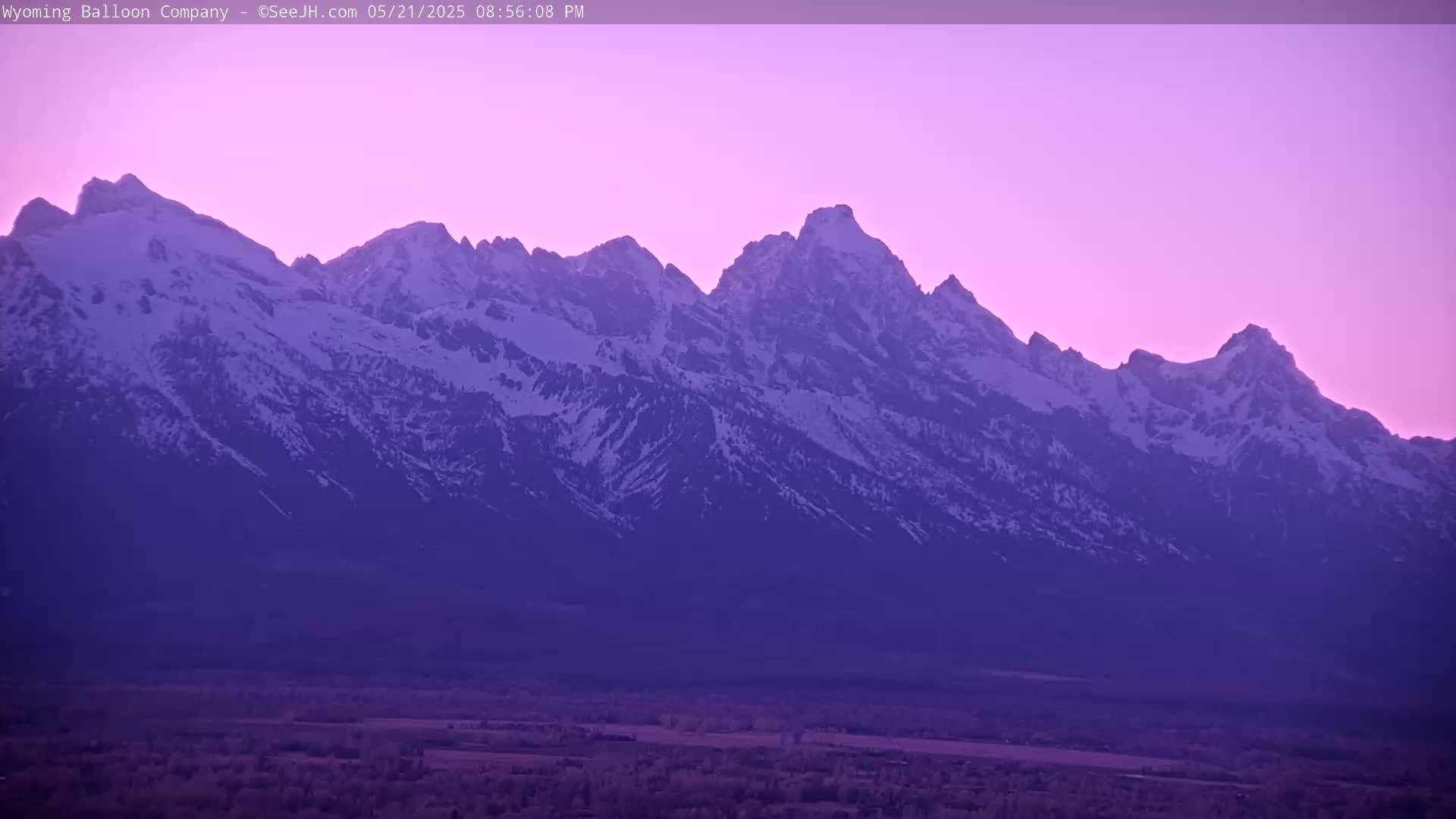 A snow-capped mountain range is silhouetted against a purple twilight sky.
