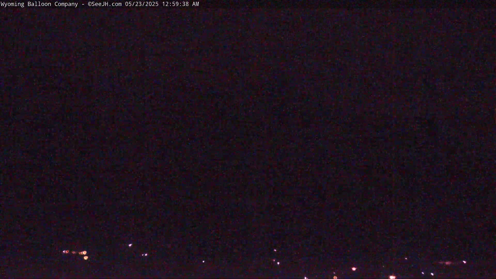 A nighttime, dark image shows a few distant lights on the horizon under a clear, dark sky.