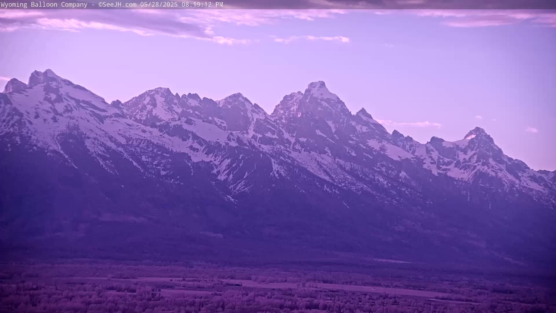 A snow-capped mountain range is seen at dusk under a mostly clear sky.