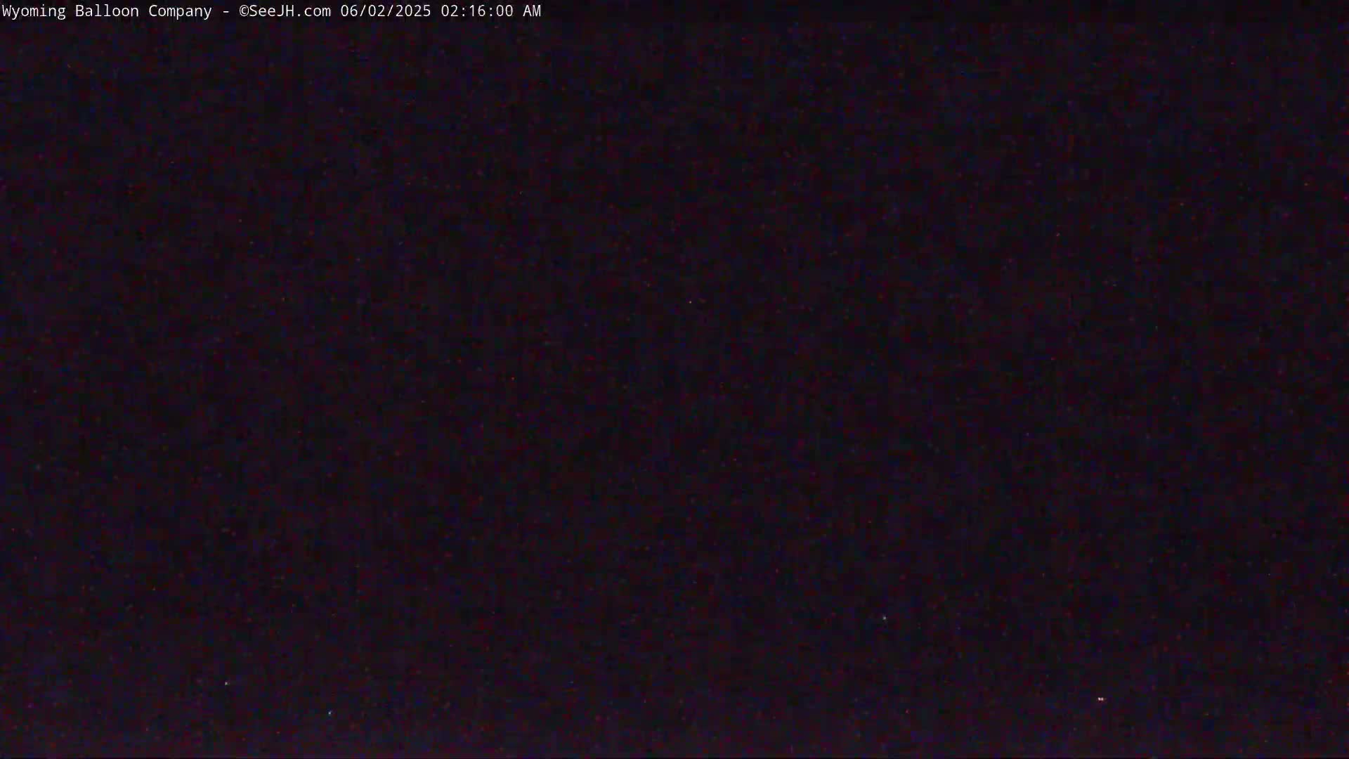 A dark, nighttime image shows a mostly uniform, very dark surface with a few specks of slightly brighter color.