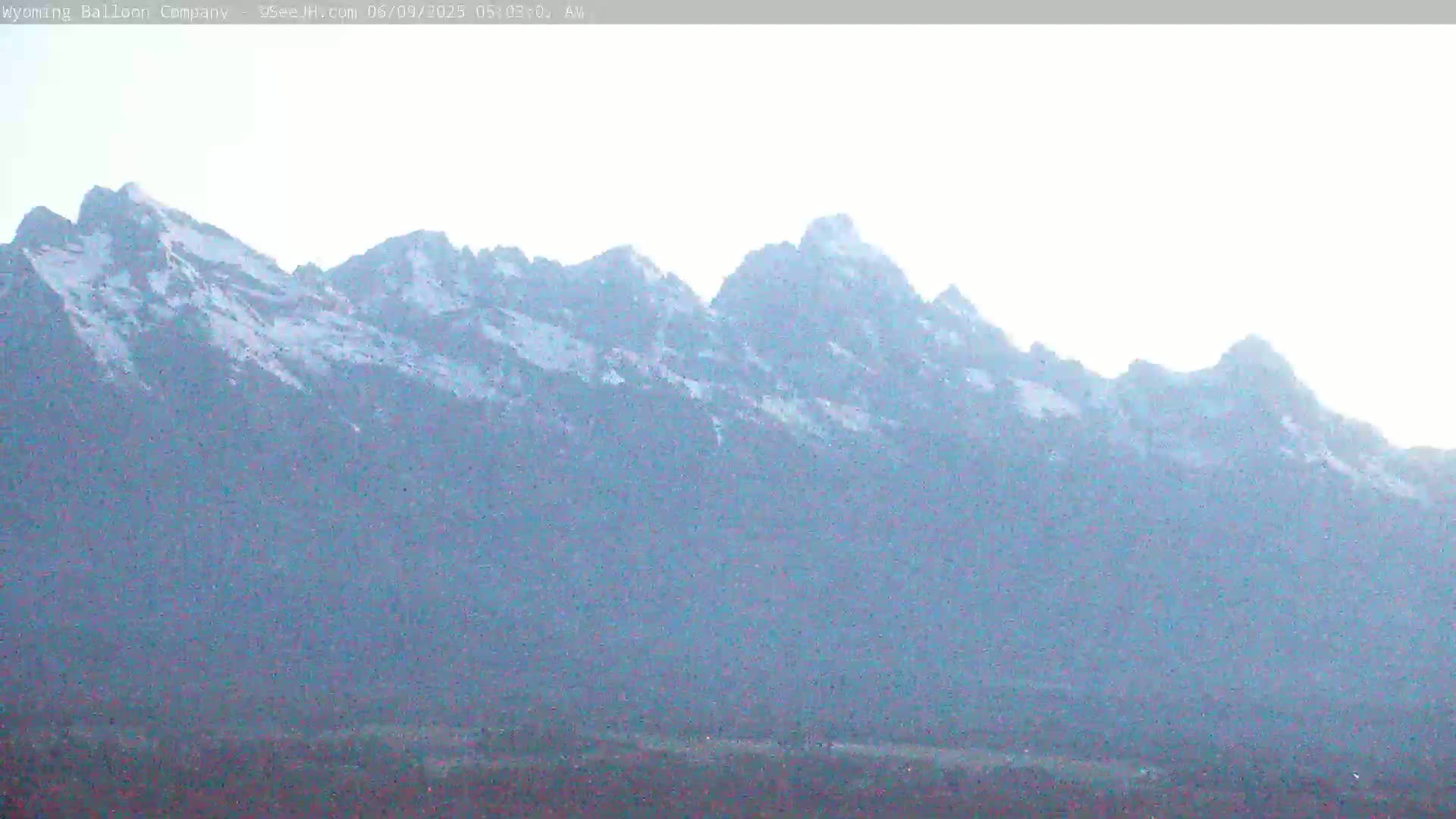 A snow-dusted mountain range is visible under a bright, hazy sky.