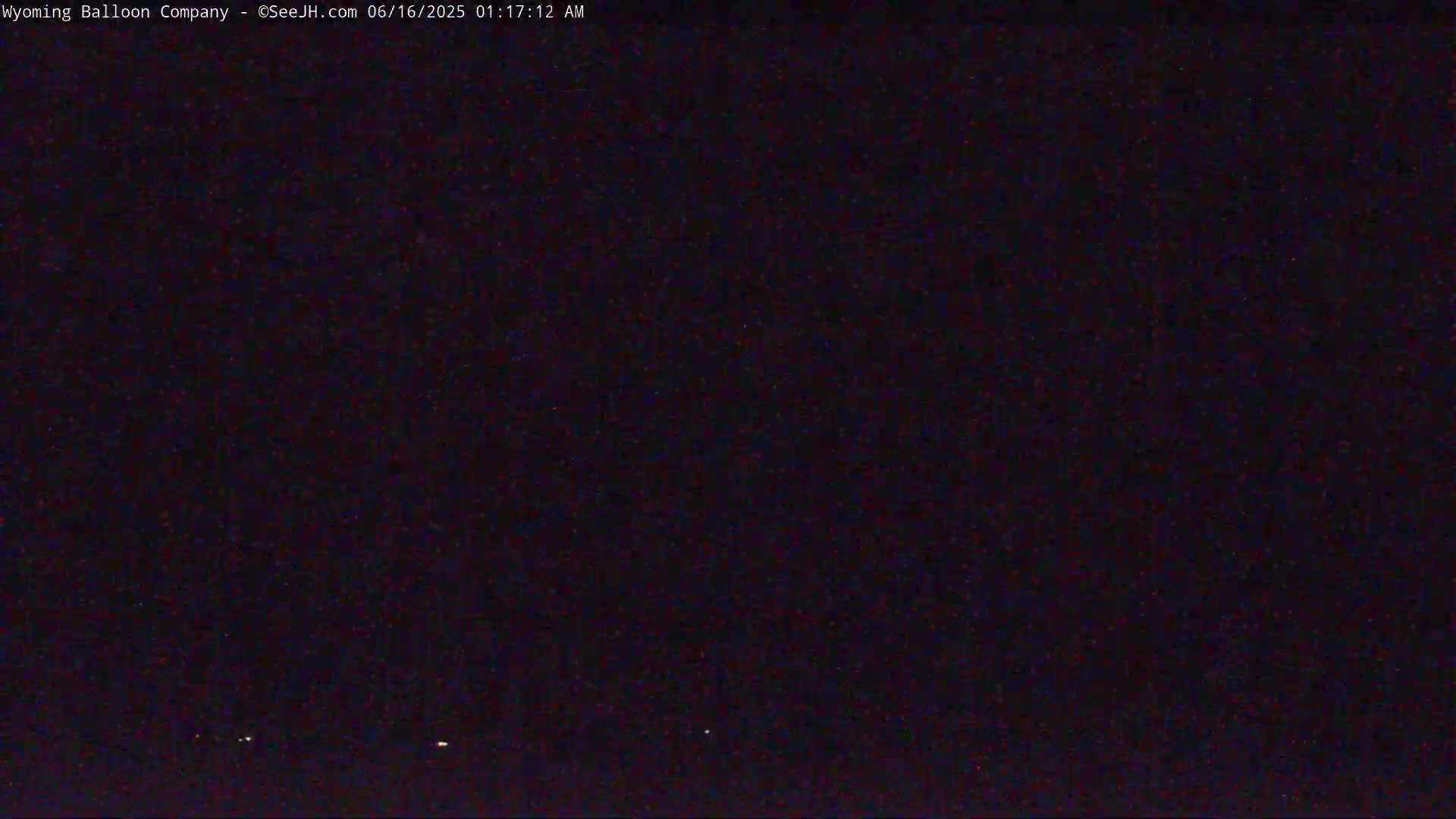 A dark, nighttime scene shows a few faint lights on the horizon.