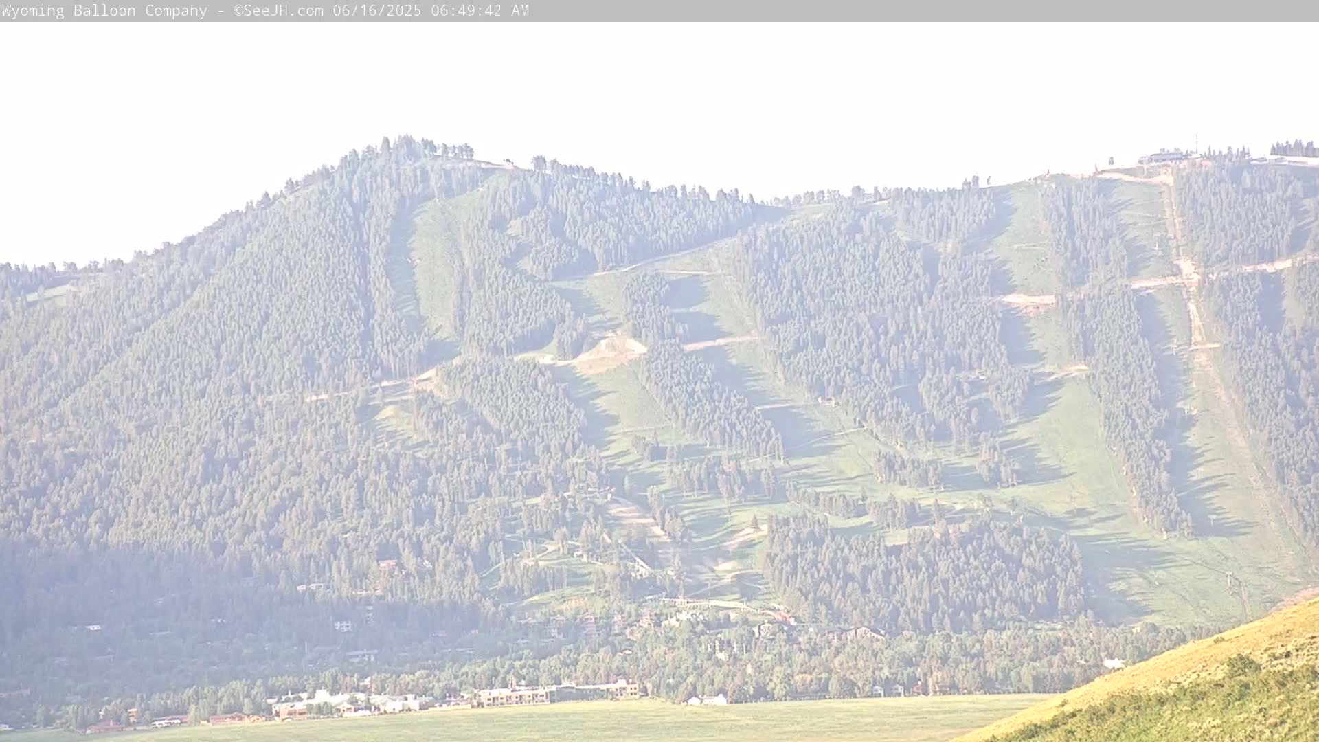 A hazy view shows a mountainside with visible ski runs and a town nestled at its base.