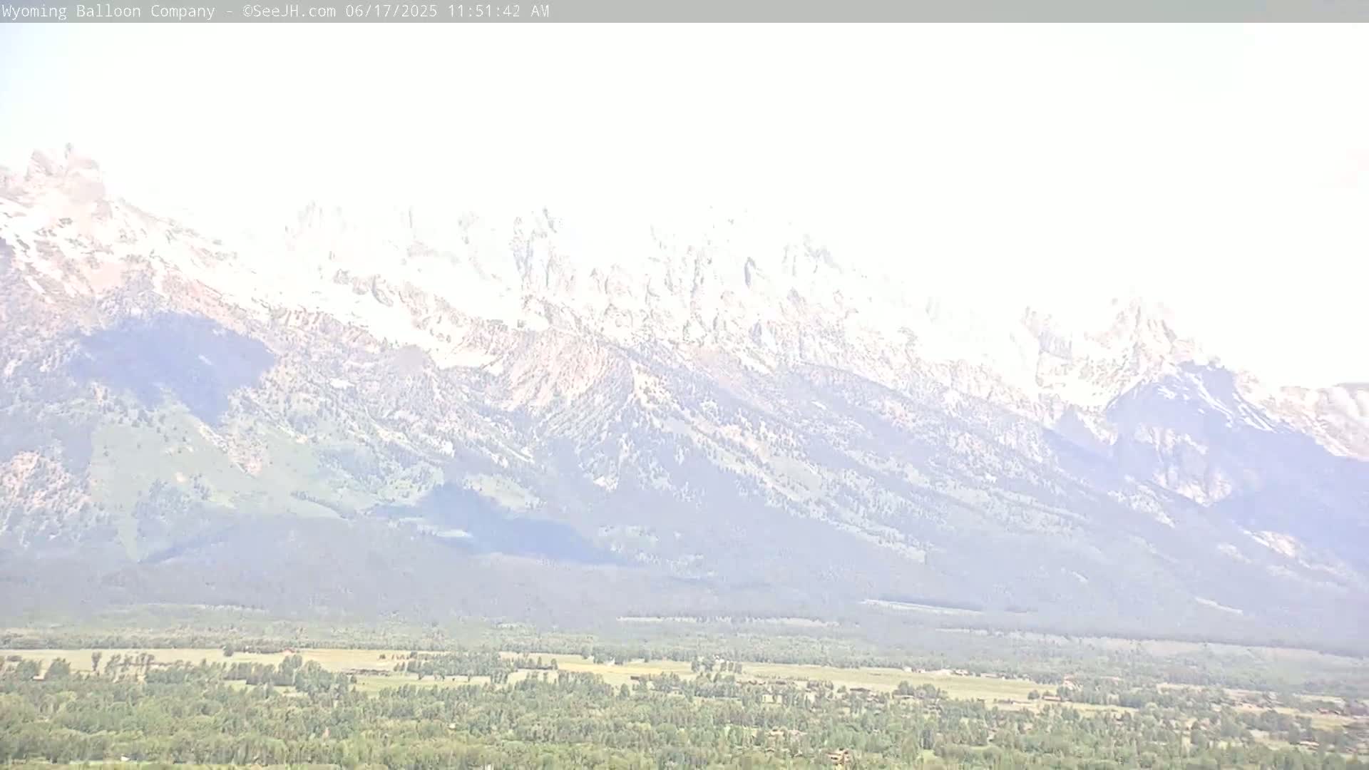A hazy, distant view shows snow-capped mountains overlooking a valley of green vegetation.