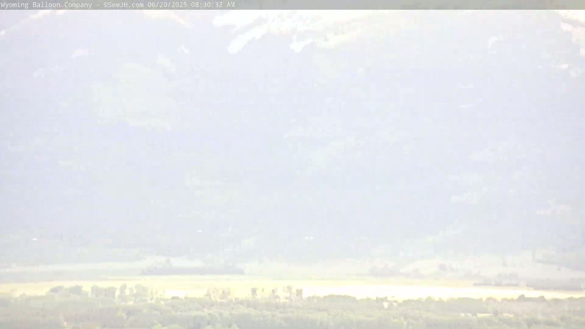 A hazy, light-colored landscape shows distant mountains and a flat expanse of land with some vegetation in the foreground.