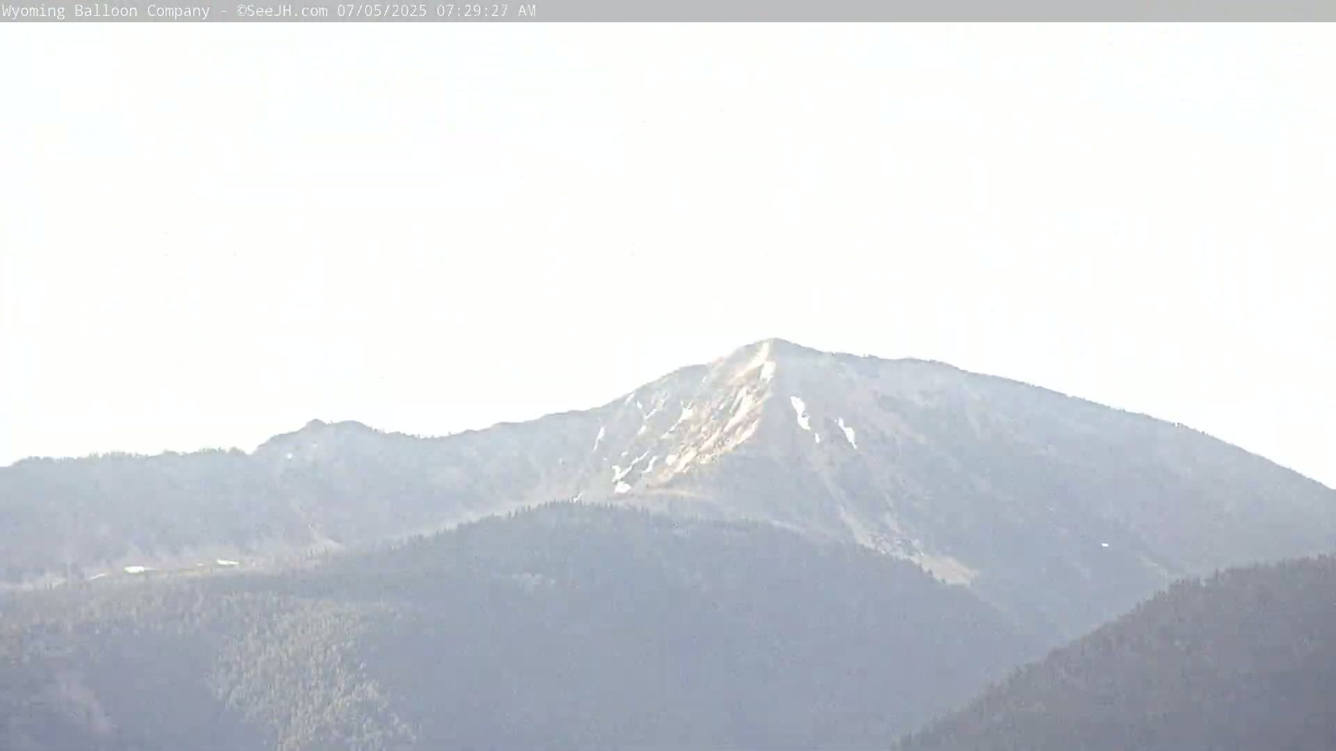 A hazy, distant mountain range with patches of snow on the highest peak is visible under a bright, mostly clear sky.