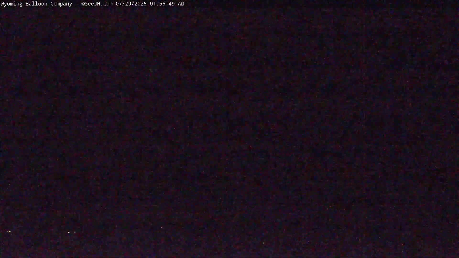A dark, nighttime image shows a mostly black field with a few tiny, faint lights.