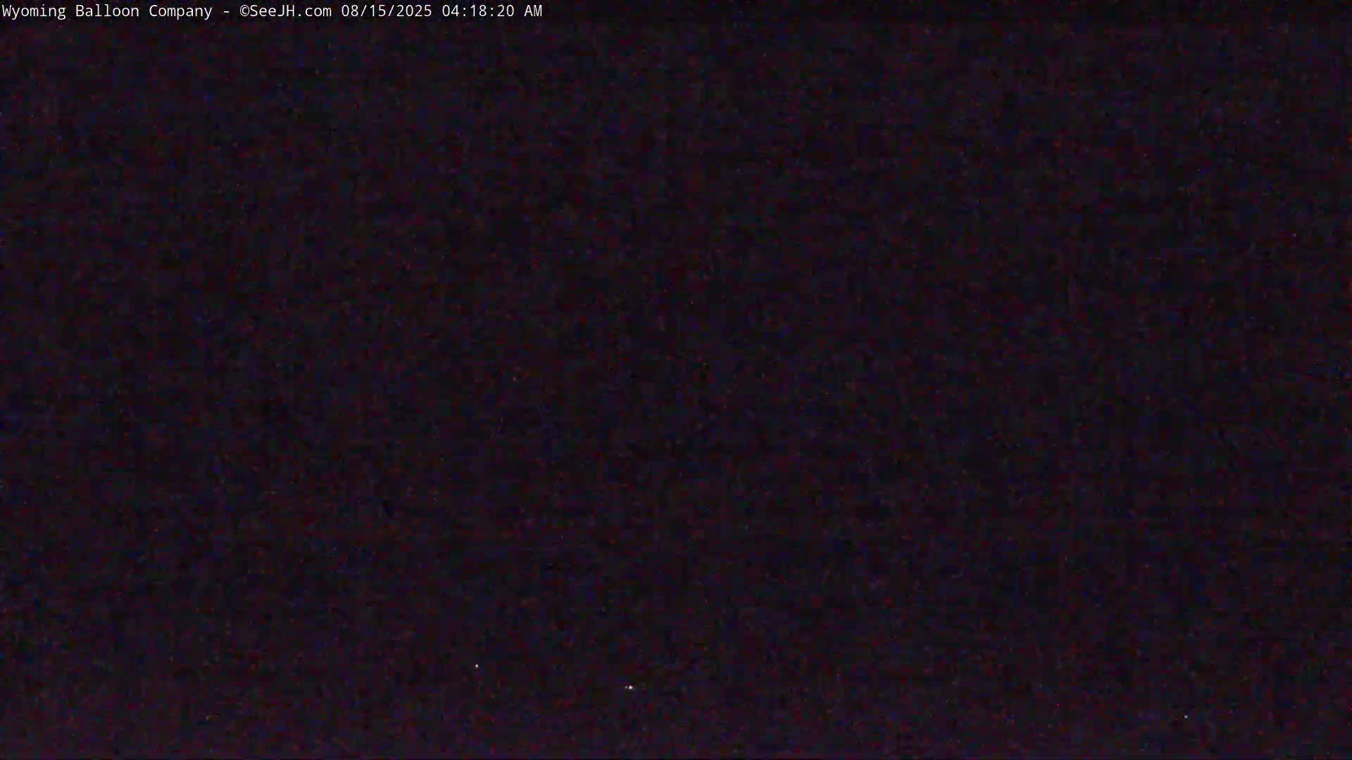 A dark, nighttime image shows a mostly black field with a few tiny, faint lights.