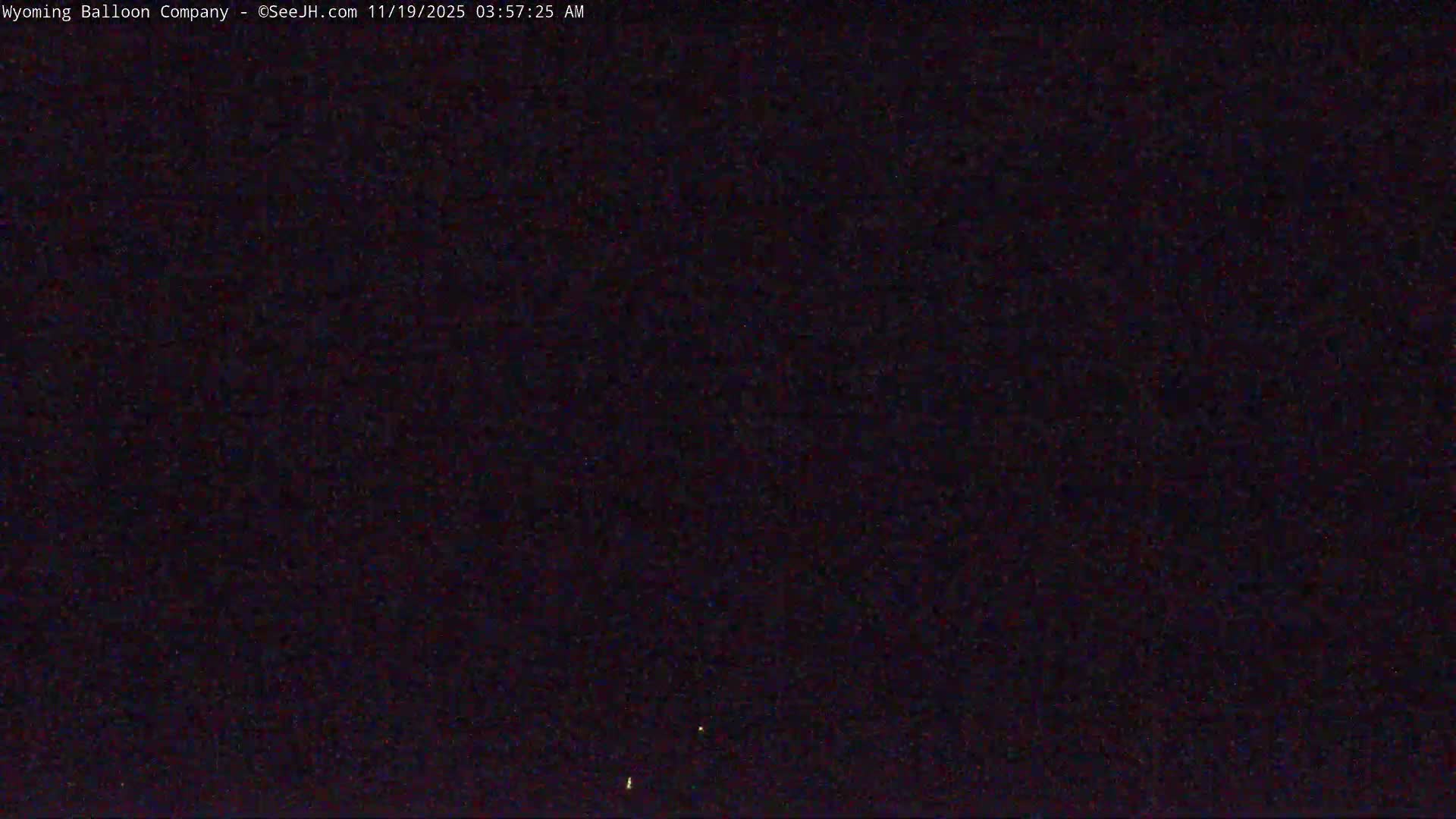 A dark, nighttime image shows a mostly black field with a few tiny, faint lights.