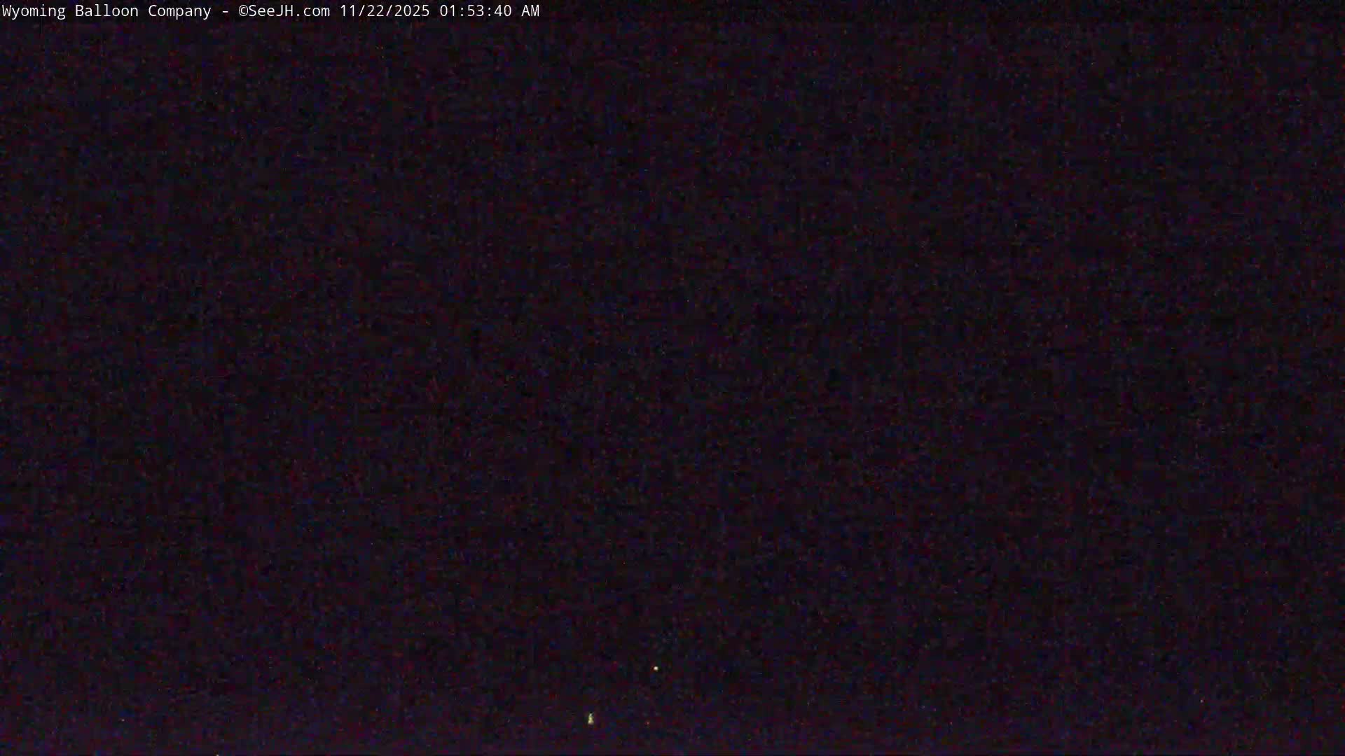 The image depicts an extremely dark and grainy outdoor night scene with a few faint lights visible near the bottom, suggesting clear sky conditions.