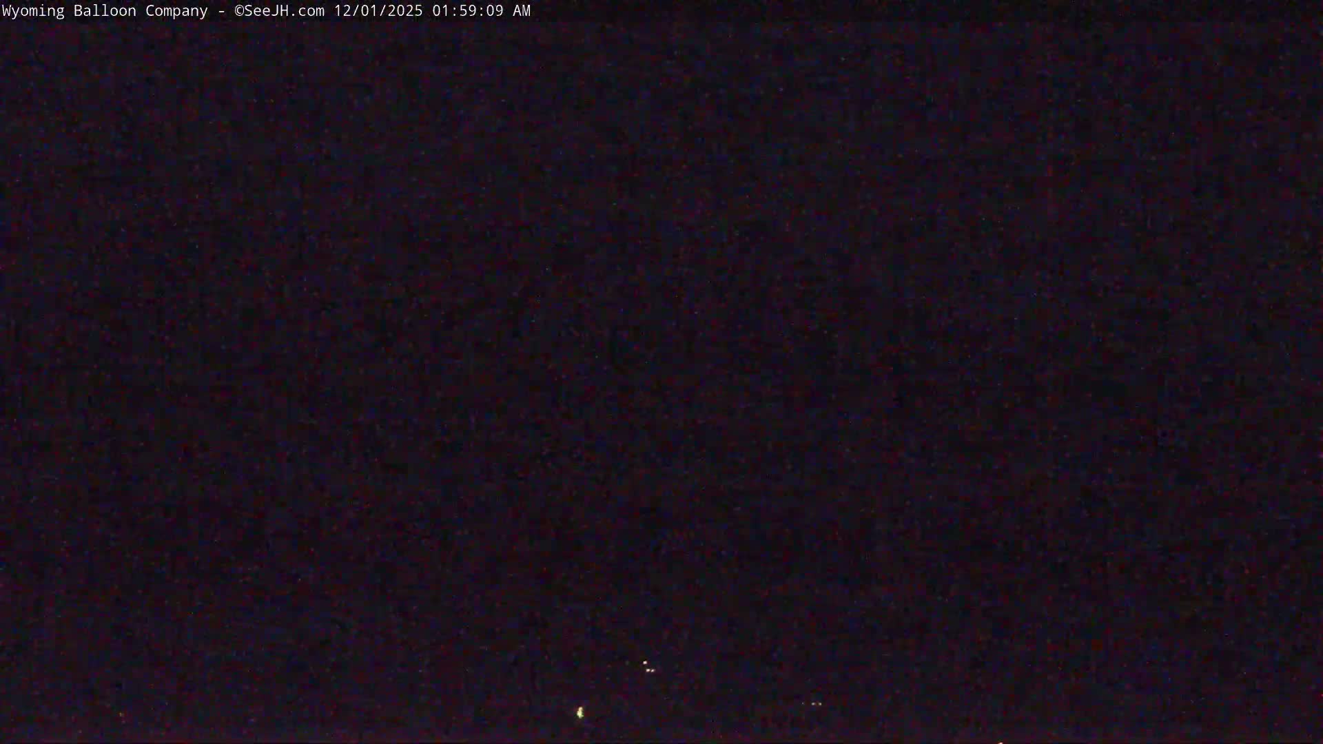 The image shows a very dark outdoor scene at night with a few faint, scattered lights visible near the bottom, under what appear to be clear skies.