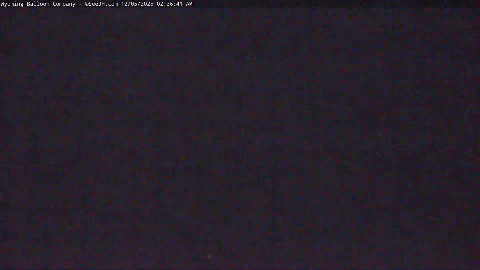 The image displays an extremely dark, almost black field with barely perceptible specks of color, indicating a pitch-black night with no visible features.