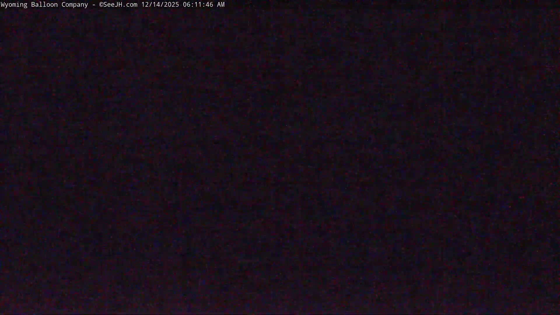 The image displays an extremely dark, almost black field with barely perceptible specks of color, indicating a pitch-black night with no visible features.