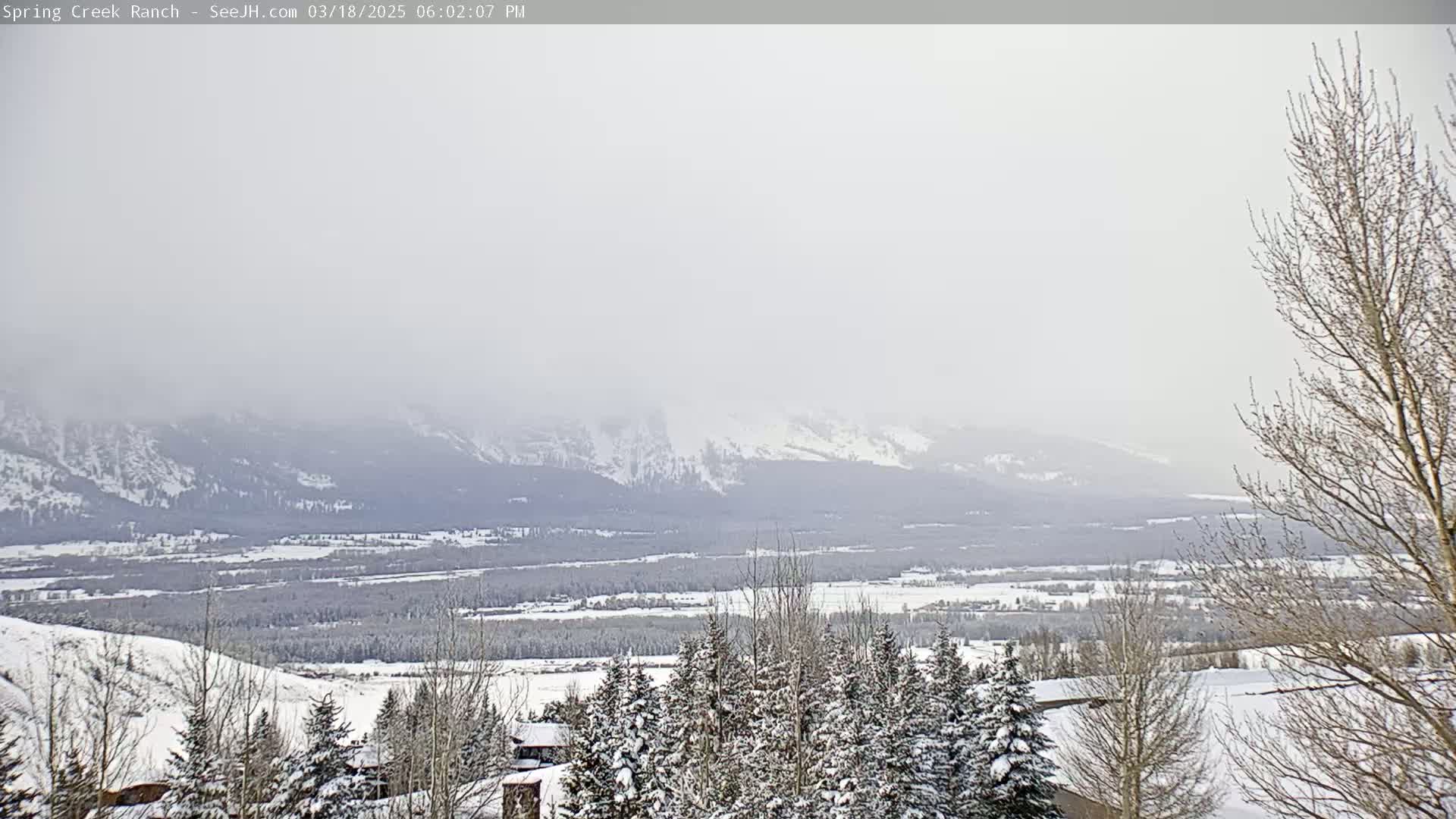 A snow-covered landscape stretches to distant, snow-capped mountains under a hazy, overcast sky.