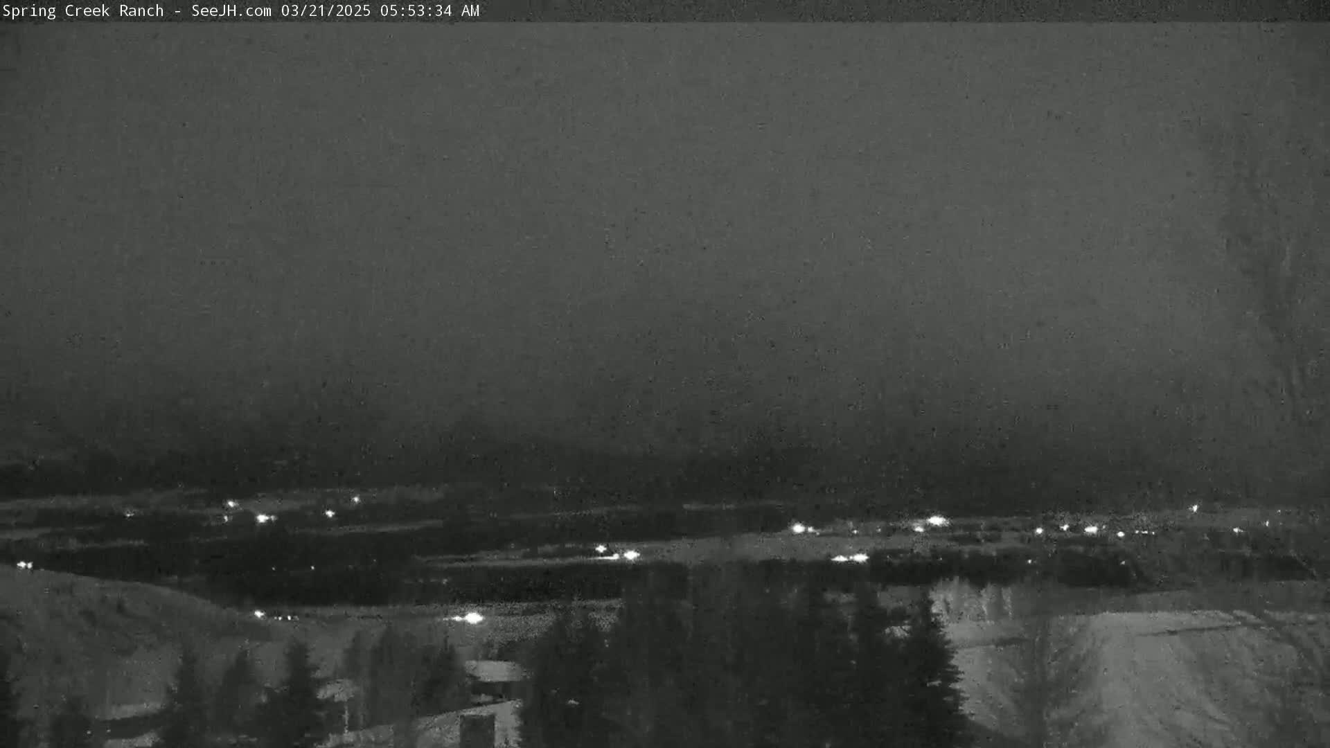 A nighttime, snowy scene shows a distant town with scattered lights below a dark, overcast sky.