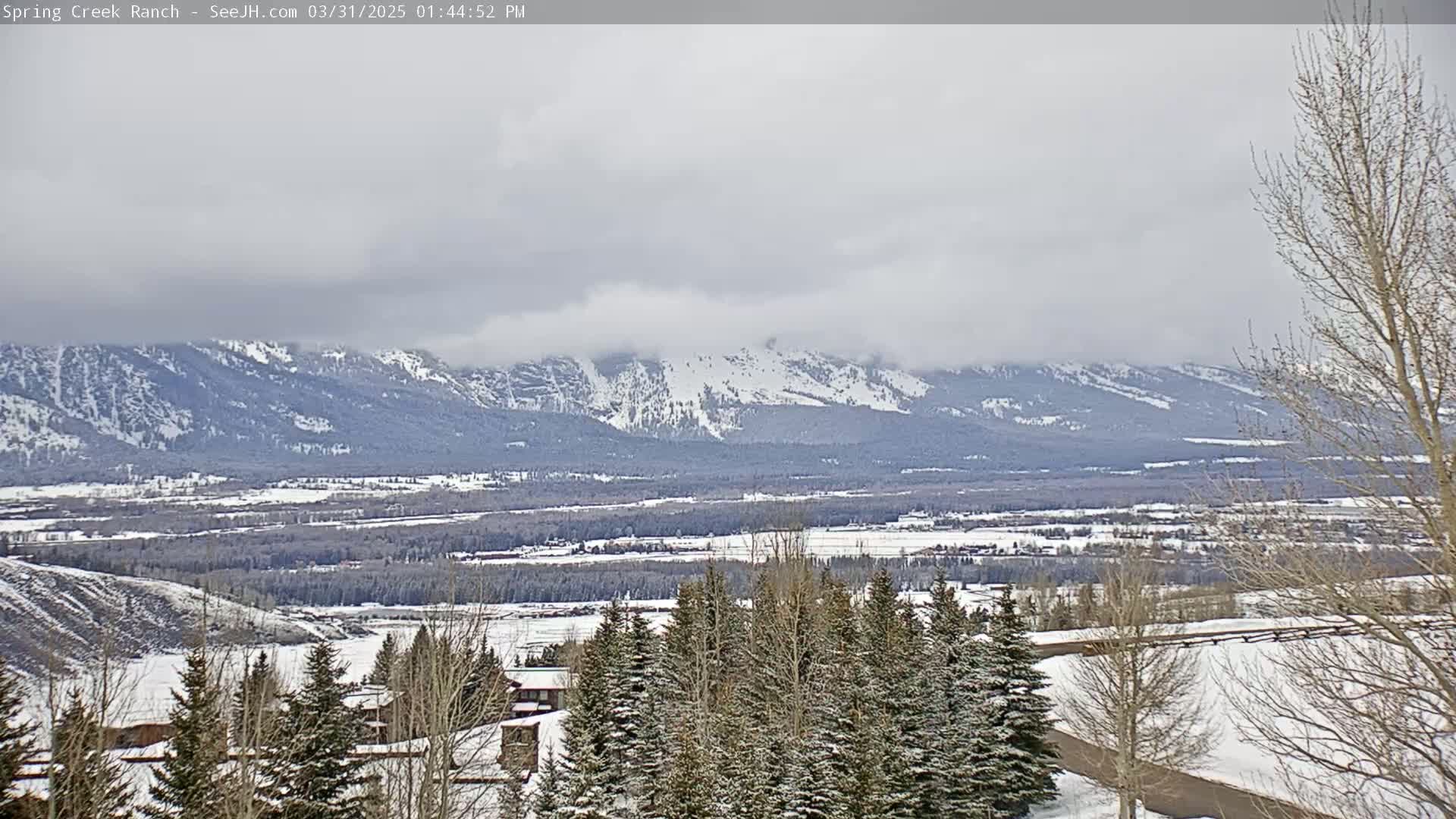 A snow-covered landscape stretches out to a range of snow-capped mountains under a cloudy sky.